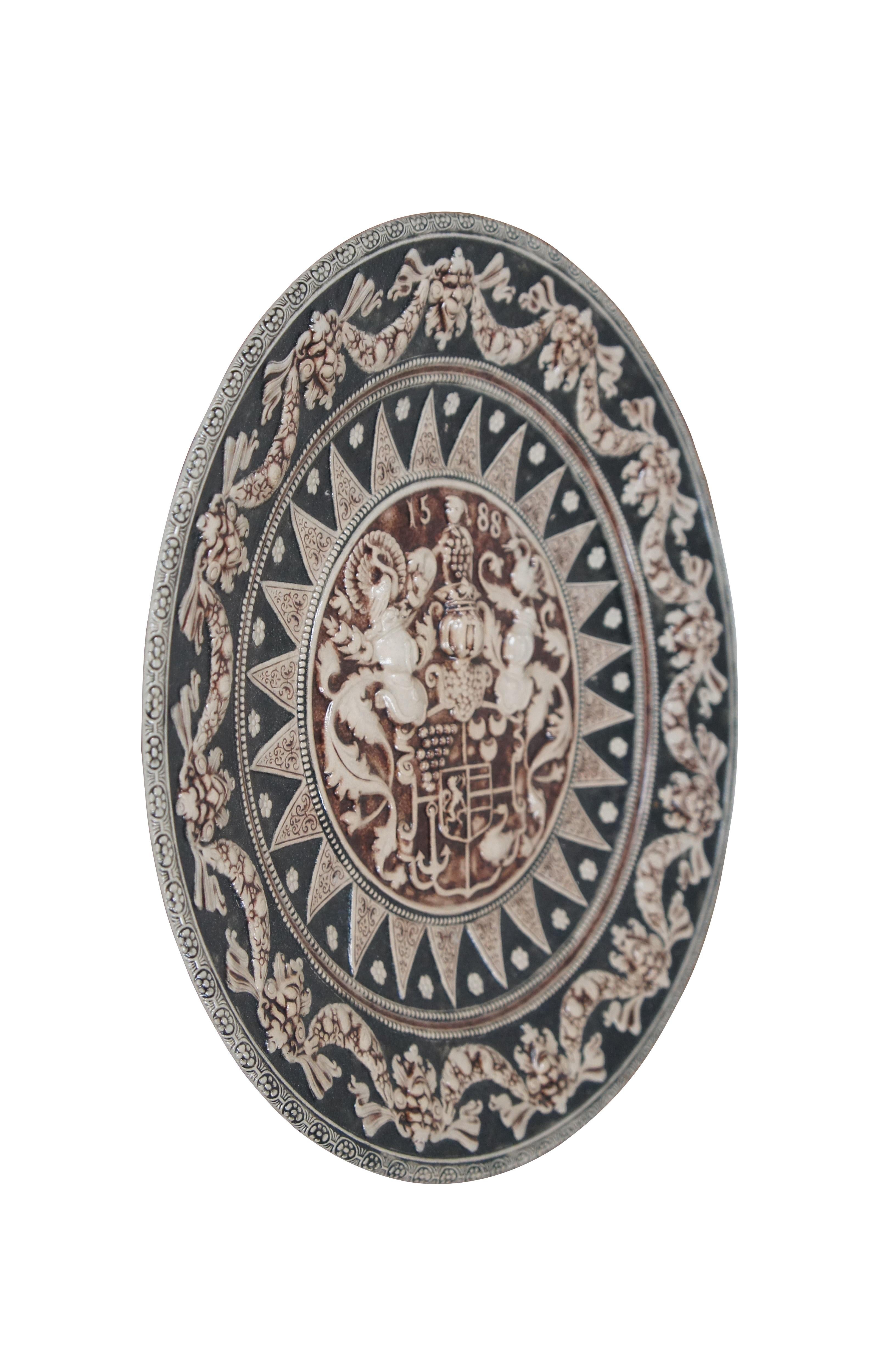 Mid to late 20th century German Westerwald salt glaze stoneware wall hanging plate / charger accented with deep charcoal and brown glaze, featuring a heraldic design in relief depicting an elaborate coat of arms festooned with plumed helmets,
