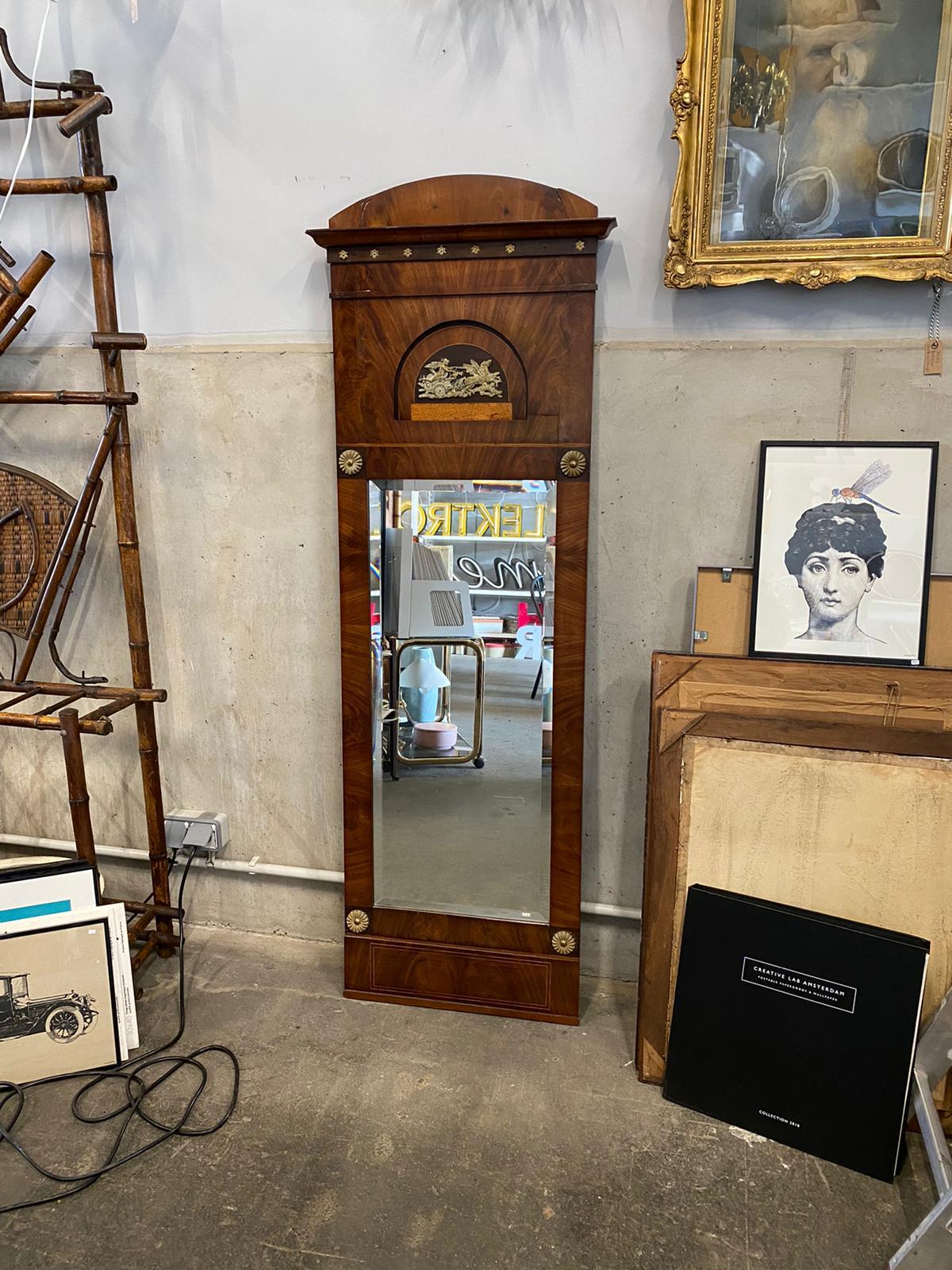 The pillar mirror, also called trumeau is from the German Biedermeier period. The frame is made of mahogany and root wood veneer. On the frame above the mirror is a mythological scene. Besides, brass applications in the form of small rosettes