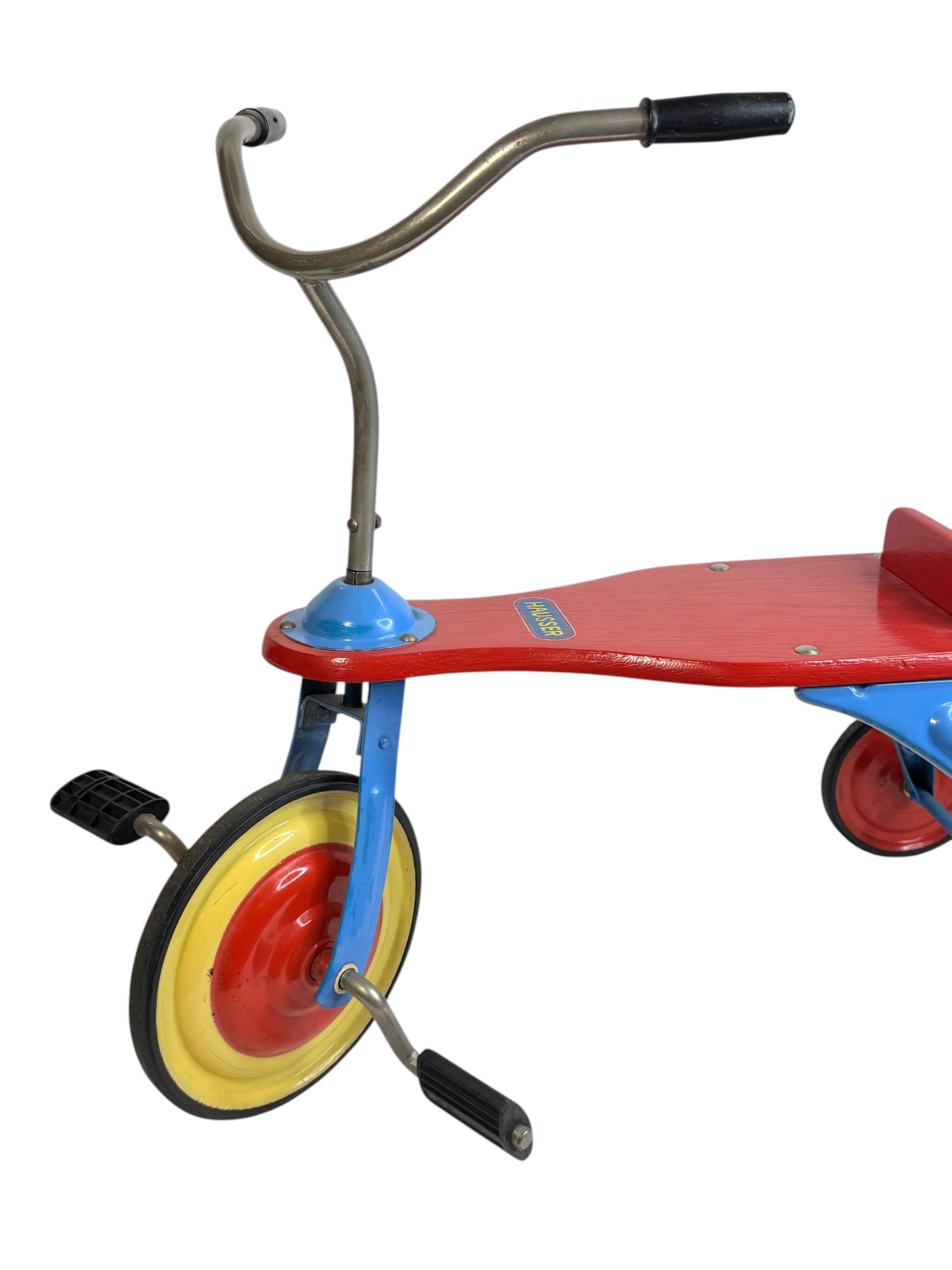 Hausser Toy Company (aussi connu sous le nom de Elastolin Figures) Allemagne tricycle d'enfant bleu rouge et beige, en fer, tôle et tubes -
Ce tricycle est équipé de petites pédales rotatives sur la roue avant, d'un large siège fixe en bois rouge,