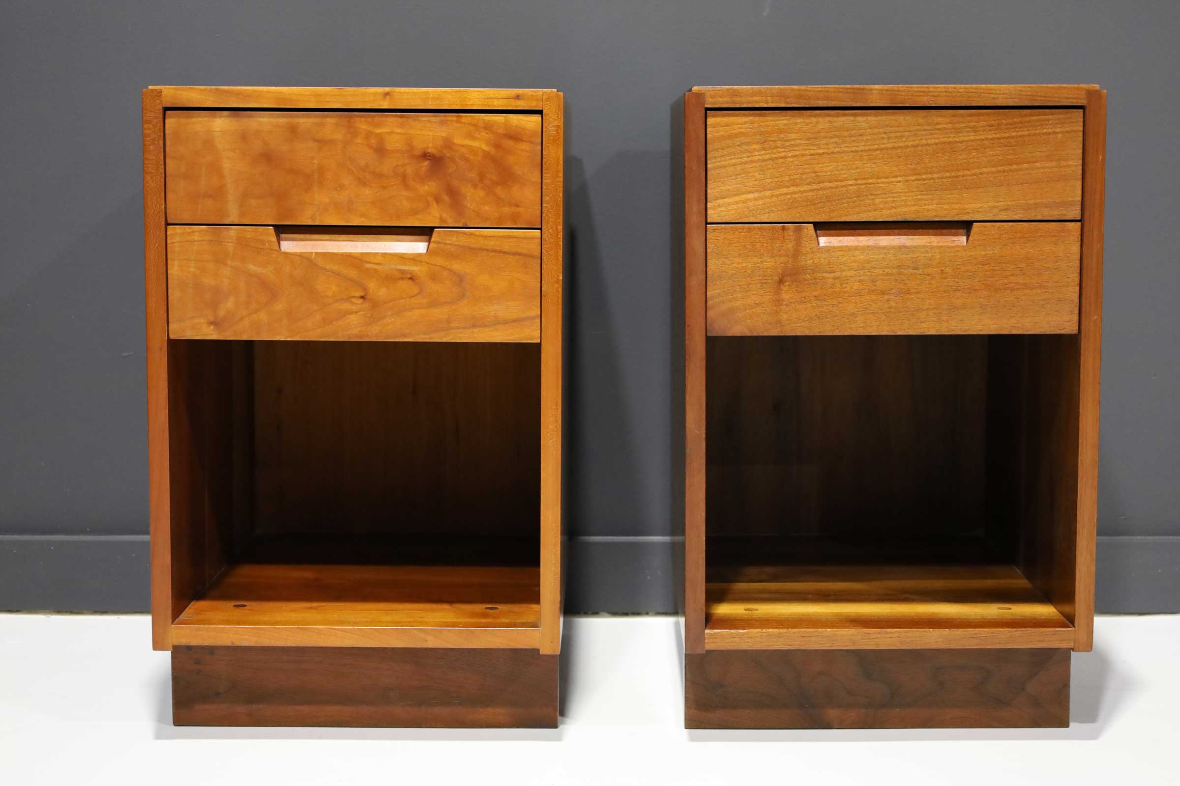 A pair of George Nakashima cherry and walnut nightstands with subsap on top and sides. Each nightstand has two upper drawers and a lower opening, toe base.