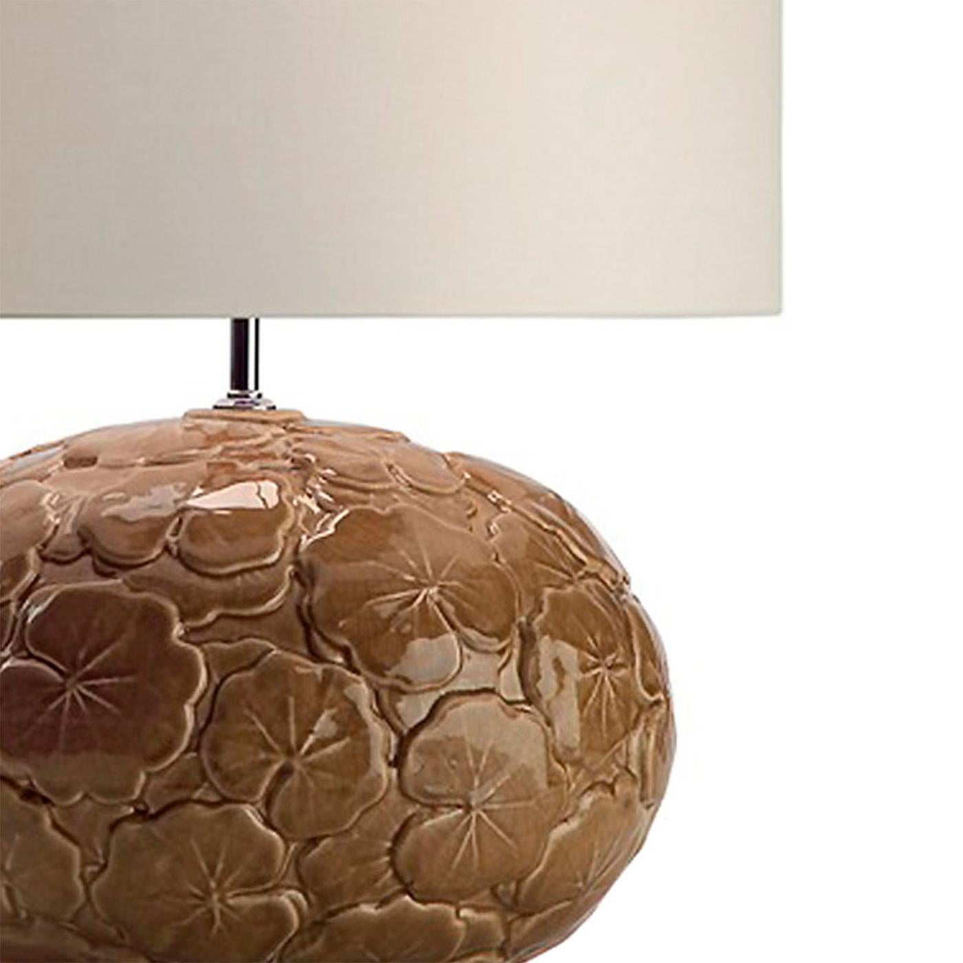 Sormontata da un classico paralume in tessuto a tamburo di immancabile raffinatezza, un corpo ovale in ceramica rigonfia decorato con un intricato motivo di foglie in rilievo conferisce a questa lampada da tavolo il suo tocco artistico. La tonalità