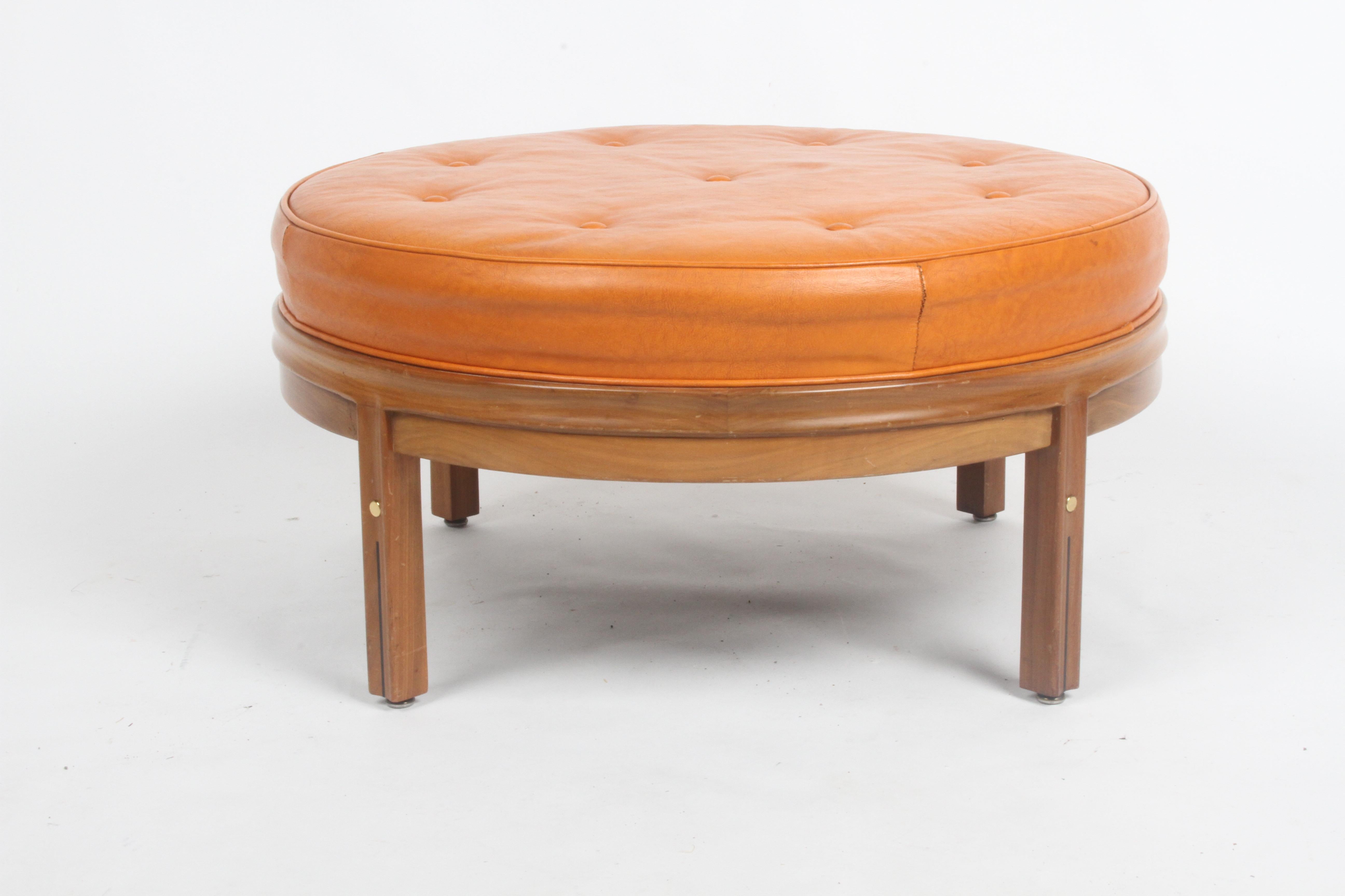 All original Mid-Century Modern round orange leather ottoman on sculpted wood base with tufted seat, designed by Gerry Zanck for Gregori furniture of Shelbyville, Indiana. Sculpted wood frame, with brass inserts and black inlay on legs. Original