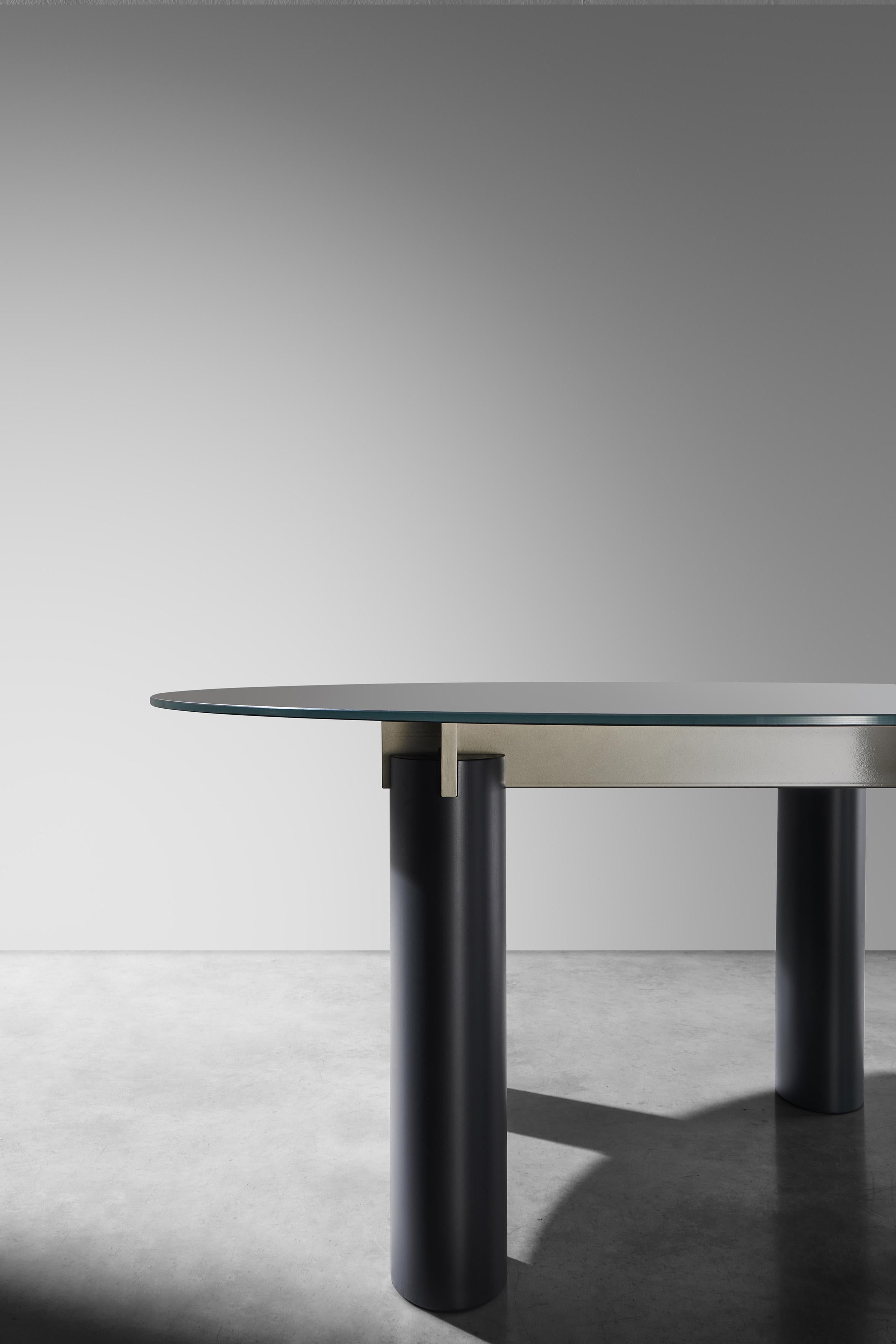 Oval table, fixed top available in the following options: 6 mm porcelain stoneware combined with 6 mm bronze-coloured glass; 12 mm glass painted; white Carrara marble top 20 mm. Lacquered MDF wood feet. Glossy lacquered steel frame.