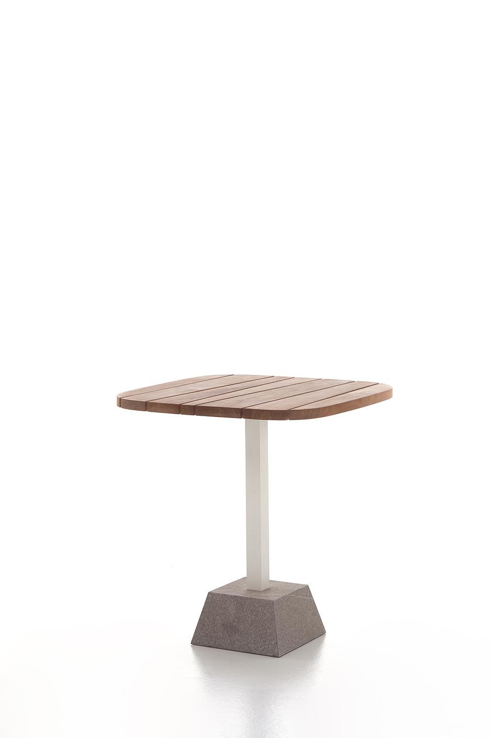Un design épuré définit la table basse Inout 137 : réalisée avec une base en pierre de Piasentina flammée, elle combine l'aluminium peint blanc, gris ou sauge de la colonne centrale, avec le plateau carré disponible en lattes de teck naturel, en