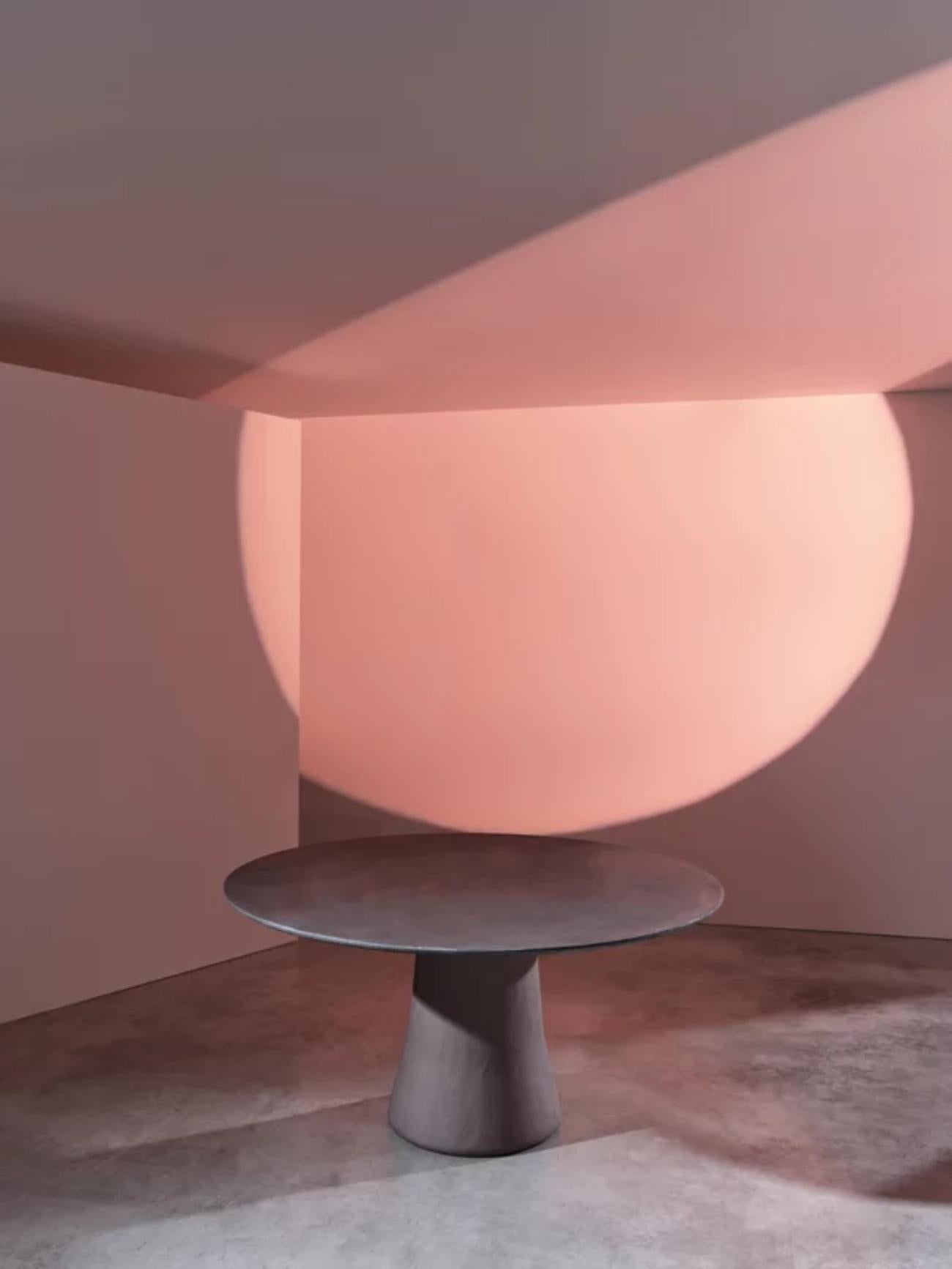 La mesa Mae, diseñada por Marco Acerbis, traslada al interior la elegancia escultural de la colección Noa. Con una base cónica afilada y un refinado acabado de arcilla caliza aplicado a mano, está disponible en versiones ovalada y redonda. La
