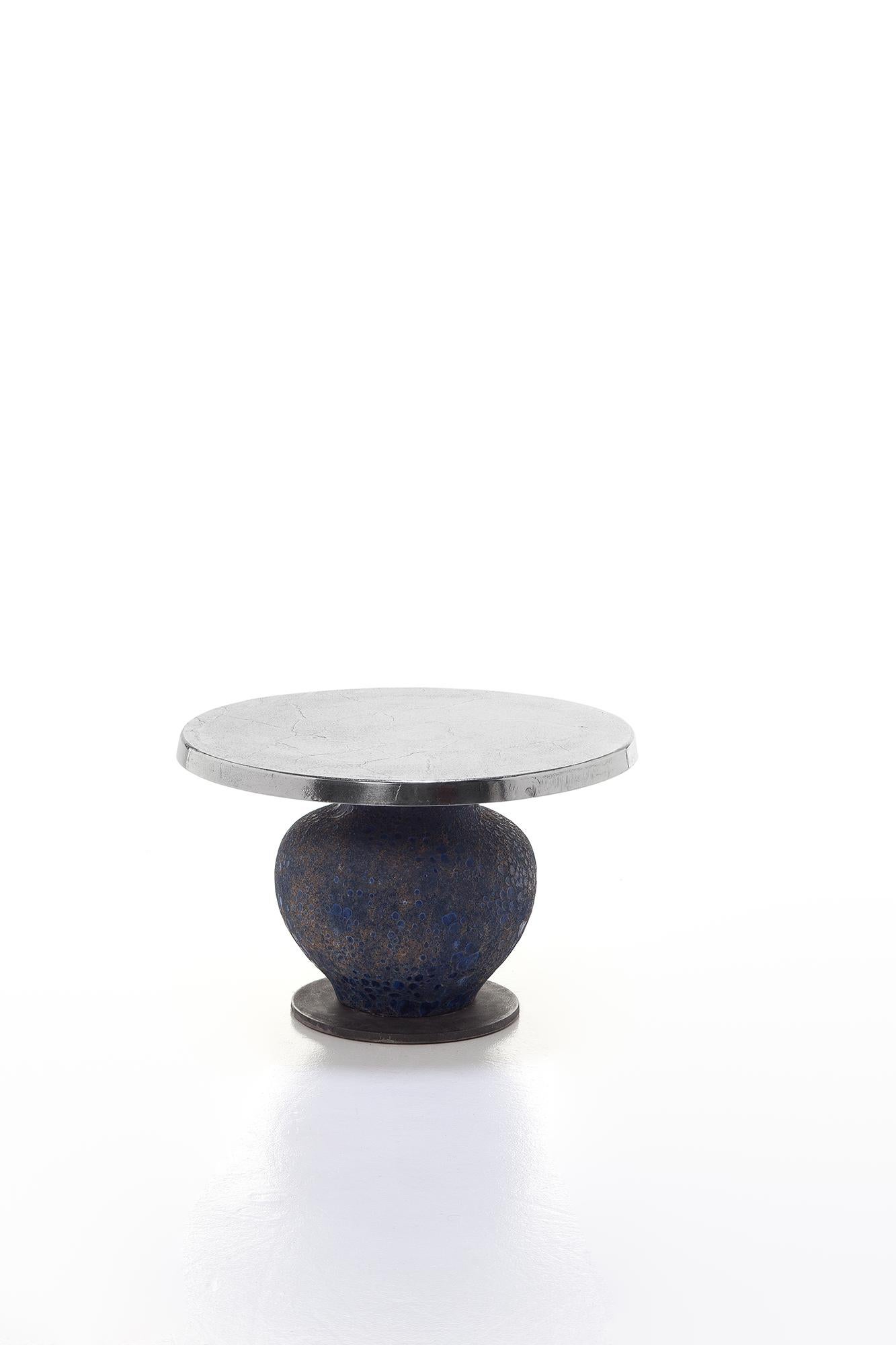 La famille de tables Moon 39/40/42 se distingue par une audacieuse combinaison de matériaux : disponibles en différentes tailles, elles sont dotées d'une base en céramique bleue en forme d'amphore, plus ou moins allongée selon la hauteur du produit,