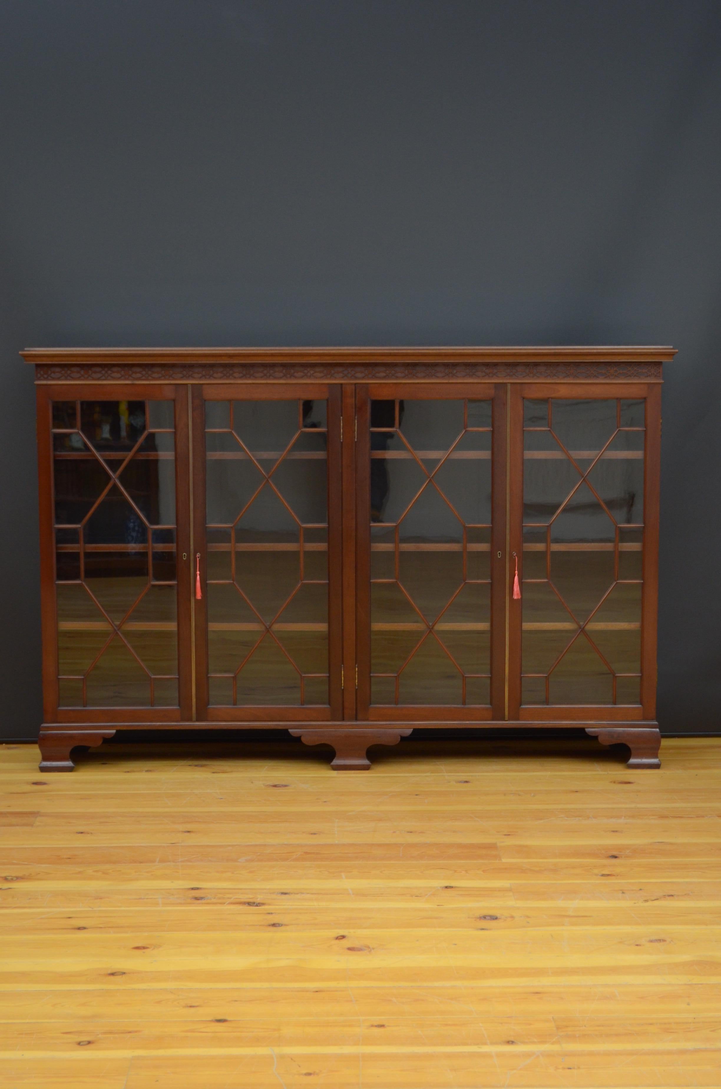 R06 A large Edwardian mahogany bookcase, having figured top with moulded edge above Chippendale style carved frieze and two pairs of astragal glazed doors both fitted with working locks and keys and enclosing height adjustable shelves, all standing