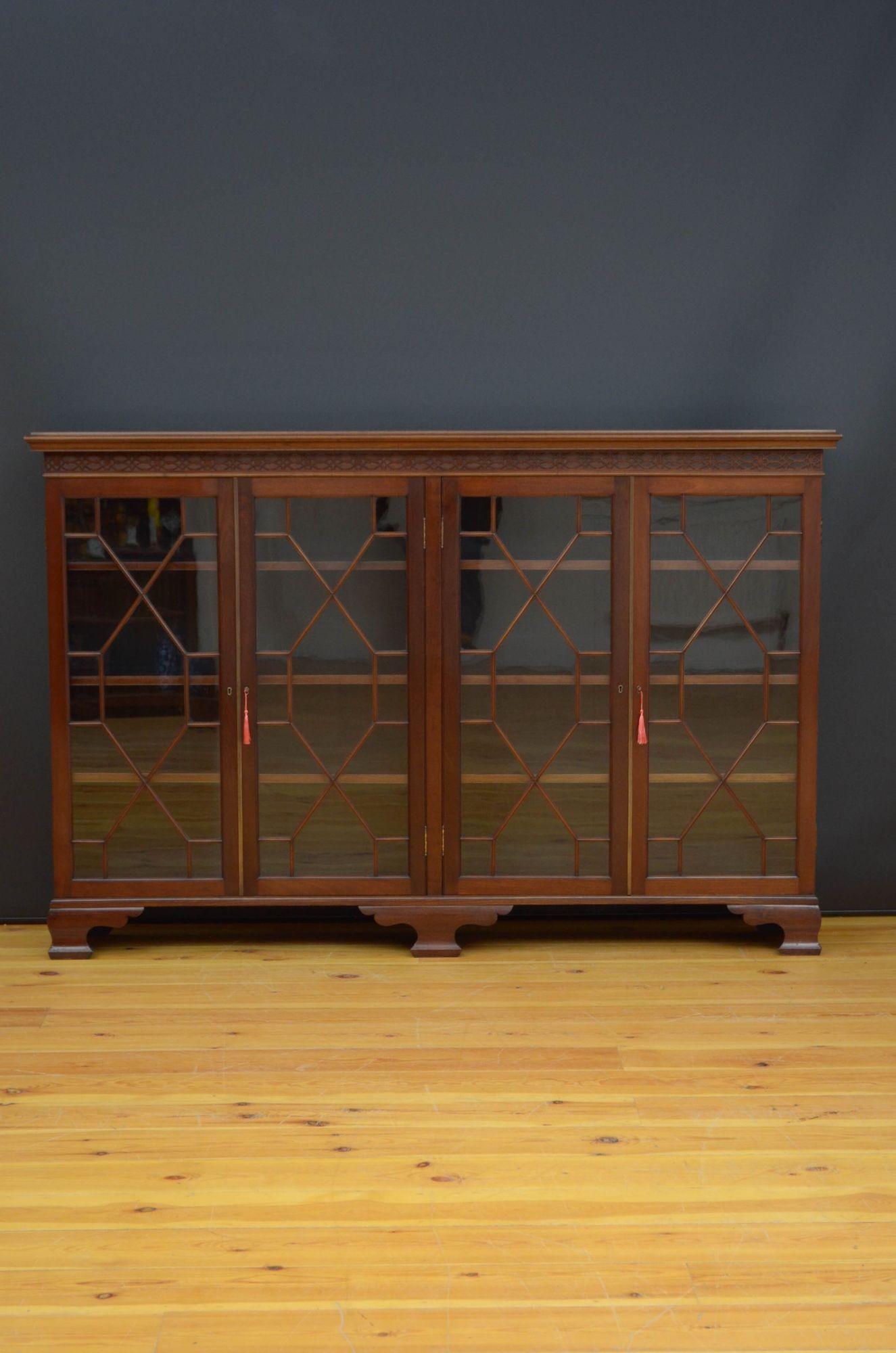 R06 A large Edwardian mahogany bookcase, having figured top with moulded edge above Chippendale style carved frieze and two pairs of astragal glazed doors both fitted with working locks and keys and enclosing height adjustable shelves, all standing