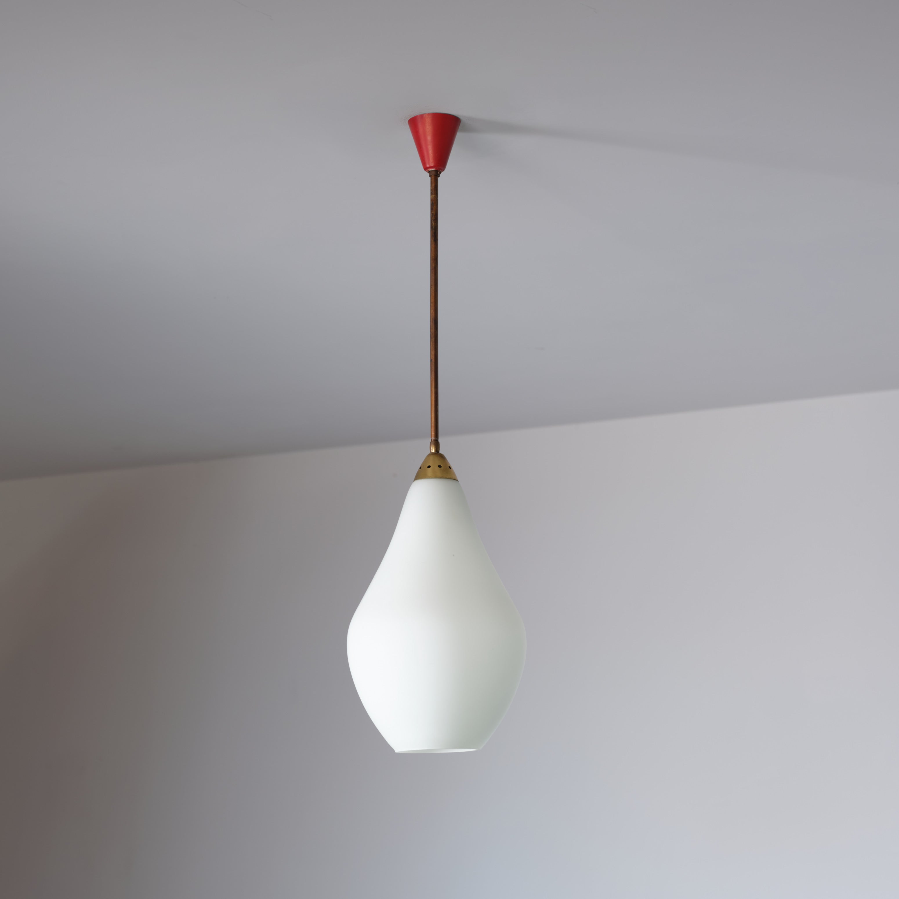 Lámpara colgante italiana de los años 50, con estructura de latón con marcas de oxidación natural desarrolladas con el tiempo, pantalla de cristal opalino y dosel de metal lacado en rojo. La combinación de materiales y acabados refleja la refinada