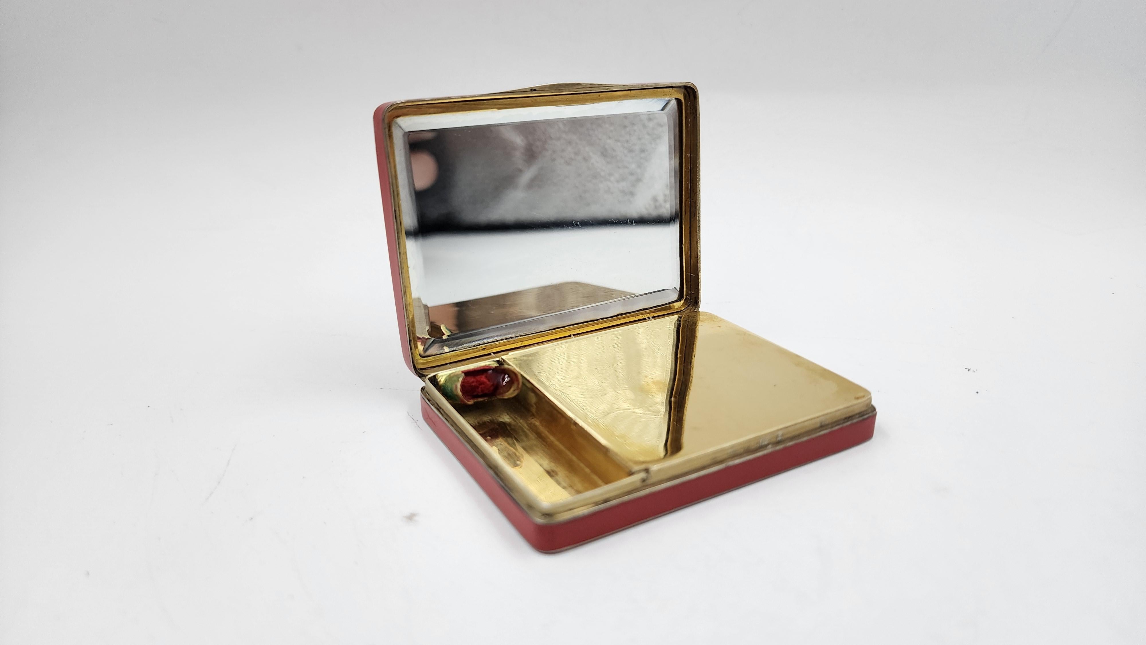 Vanity Case en or de Ghiso avec décoration en jade
Ce vanity case Art Deco de Ghiso présente un design compact et rectangulaire avec des coins légèrement arrondis. Son extérieur est recouvert d'un émail rouge vif, avec des bords en métal poli. Le