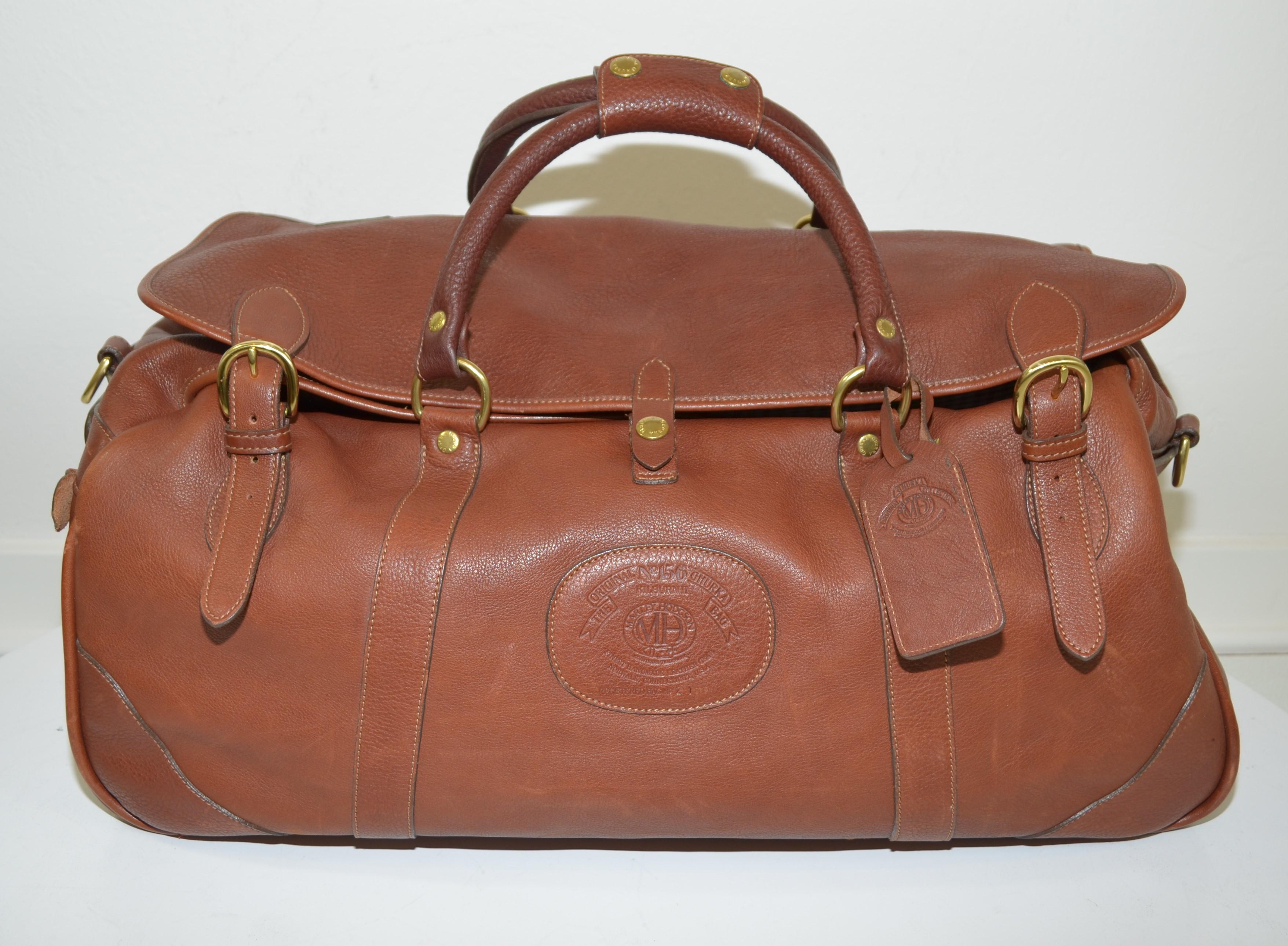 Ghurka Vintage Cavalier Leather Duffel Bag with Travel Accessories -- featured in a cognac brown leather with gold-tone hardware. Duffel bag has a top dual zippered closure, flaps with velcro, and rolled top handles. Interior is fully lined in a