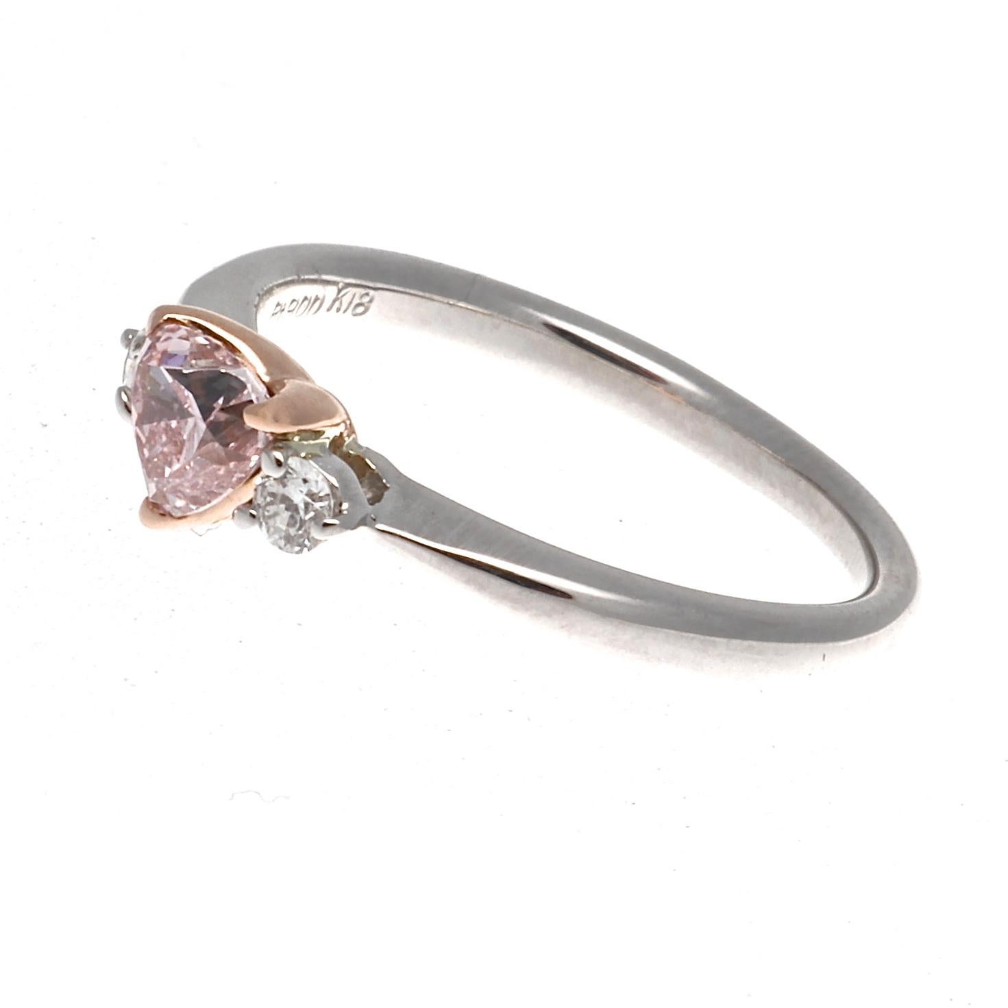 An alluring saturation of color emanates from this heart shape diamond. Featuring a GIA certified 0.45 carat heart shaped diamond that is a natural Fancy Orangy Pink color. Accented on either side by a single colorless round brilliant cut diamond.