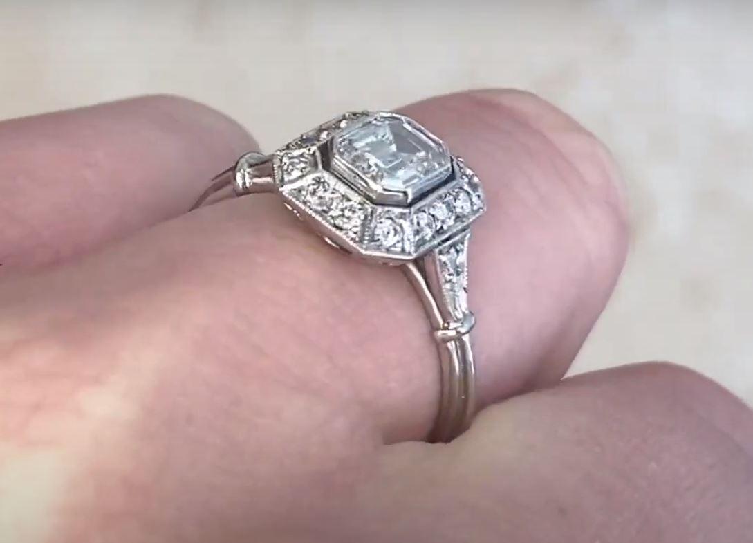 This exquisite diamond halo engagement ring showcases a GIA-certified approx. 0.70-carat emerald-cut diamond, graded H in color and VS2 in clarity. The center stone is elegantly bezel-set, offering a sleek and sophisticated presentation while