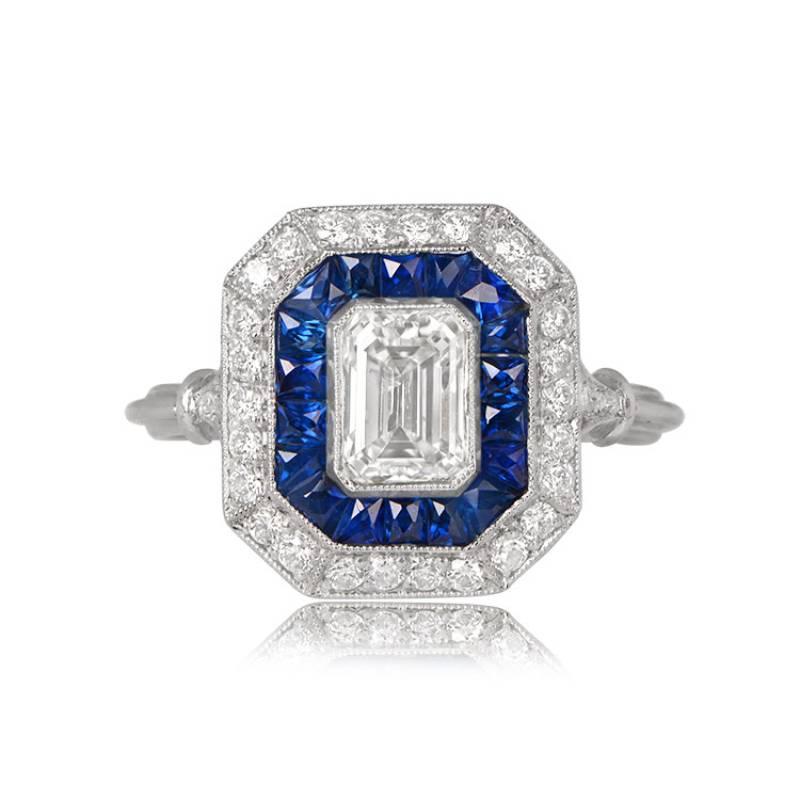 A captivating double halo ring showcases a vibrant GIA-certified 0.87-carat emerald-cut diamond. Encircling the center stone is a row of natural blue French-cut sapphires and old European cut diamonds. Hand-crafted in platinum, this ring boasts a