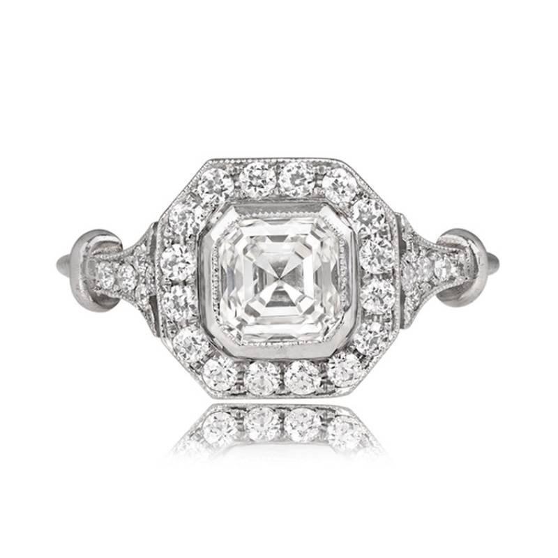 A captivating engagement ring highlights a vintage Asscher-cut diamond, elegantly set in a handcrafted platinum mounting and enhanced by a halo of antique old European cut diamonds. GIA-certified as 1.01 carats, the center diamond boasts J color and