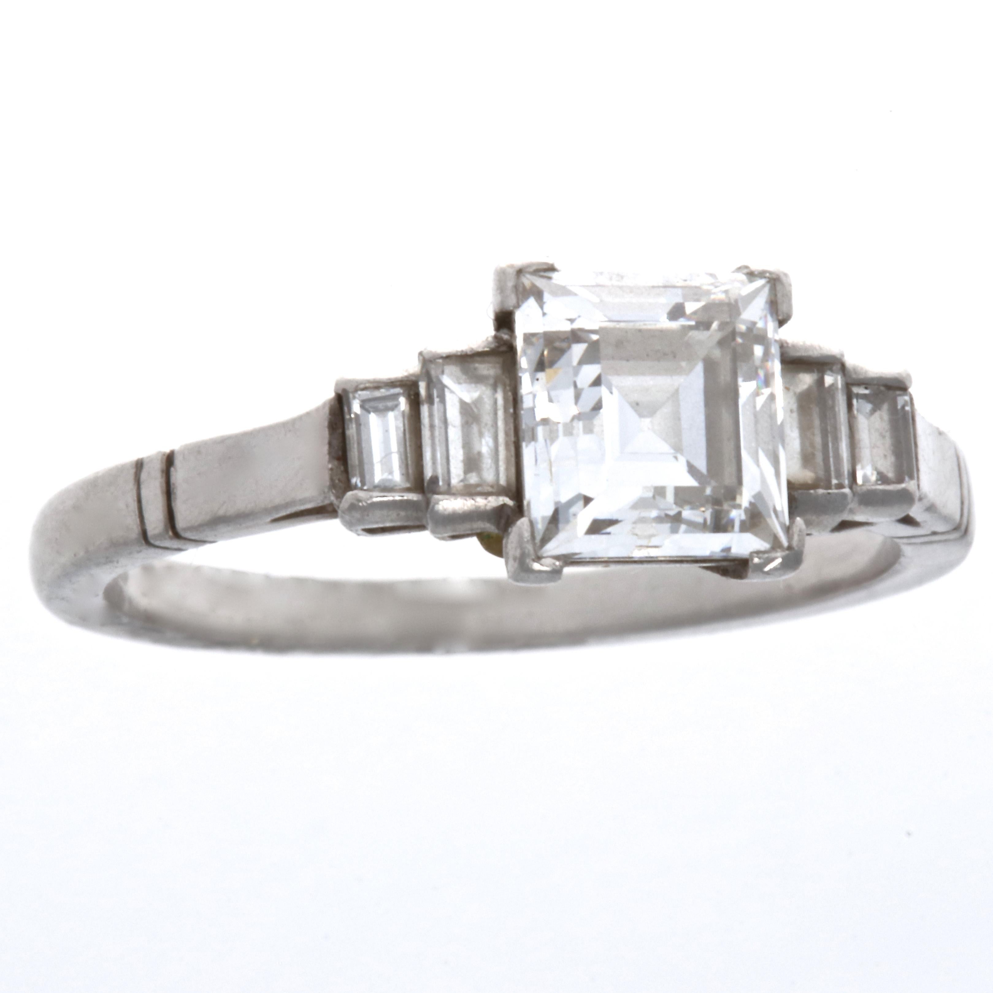 This ring is a reminder of the enduring creativity of the Art Deco era. The Art Deco style carre cut diamond is GIA certified as 1.17 carats, E color VVS2 clarity. Accented with four emerald cut diamonds weighing approximately 0.35 carats G,H color