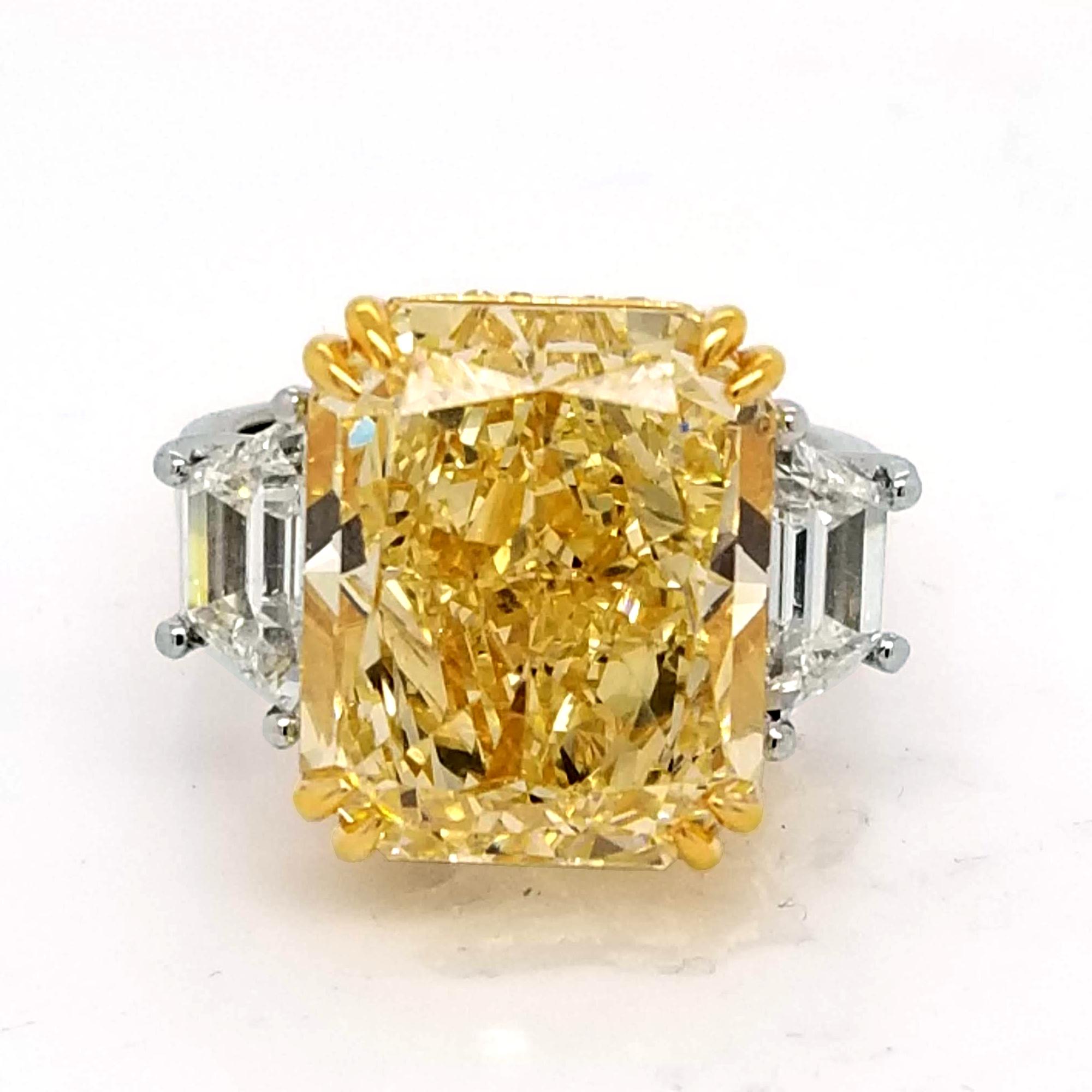 A beautiful Elongated Radiant Natural Fancy Yellow SI2 GIA certified center Diamond set in a fine Platinum with 18k Yellow gold accent 3 Stone Ring with 2 Trapezoid Cut diamonds on the side (1.31 Ct). The side of the cup is pave set with 98 pieces