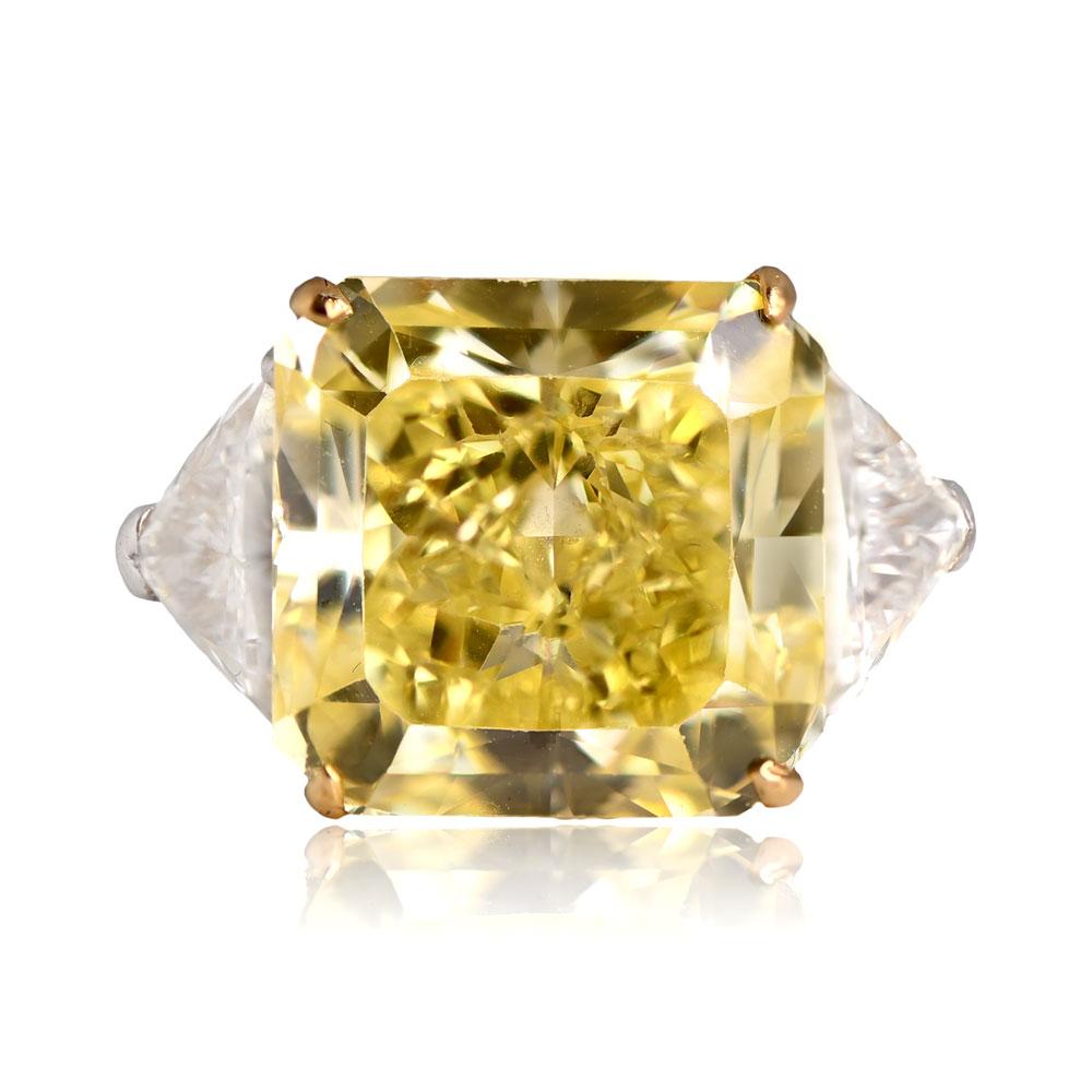 This magnificent ring showcases a GIA-certified 13.15-carat radiant-cut Fancy Intense Yellow diamond with VS1 clarity, set in yellow gold prongs and complemented by two substantial triangle-shaped diamonds. The entire composition is presented in