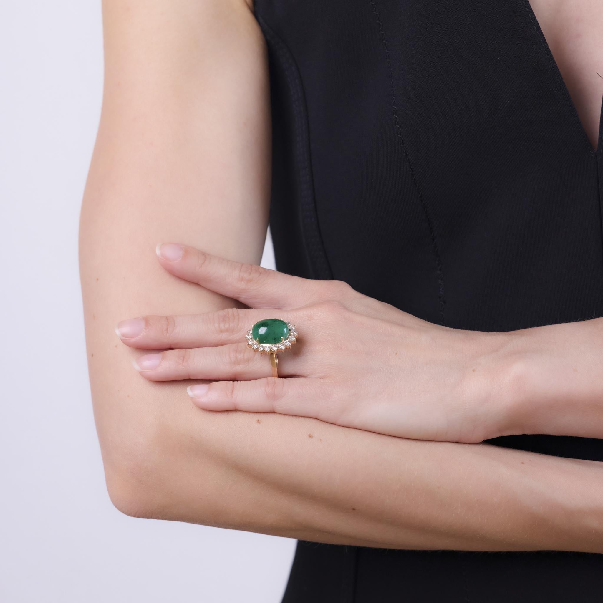 This vintage ring from the 1990s features a GIA-certified 14 carat oval double cabochon emerald of Brazilian origin (GIA #6237573590), noted as F2 for moderate clarity enhancement. Surrounding the vibrant green center stone are 18 round brilliant