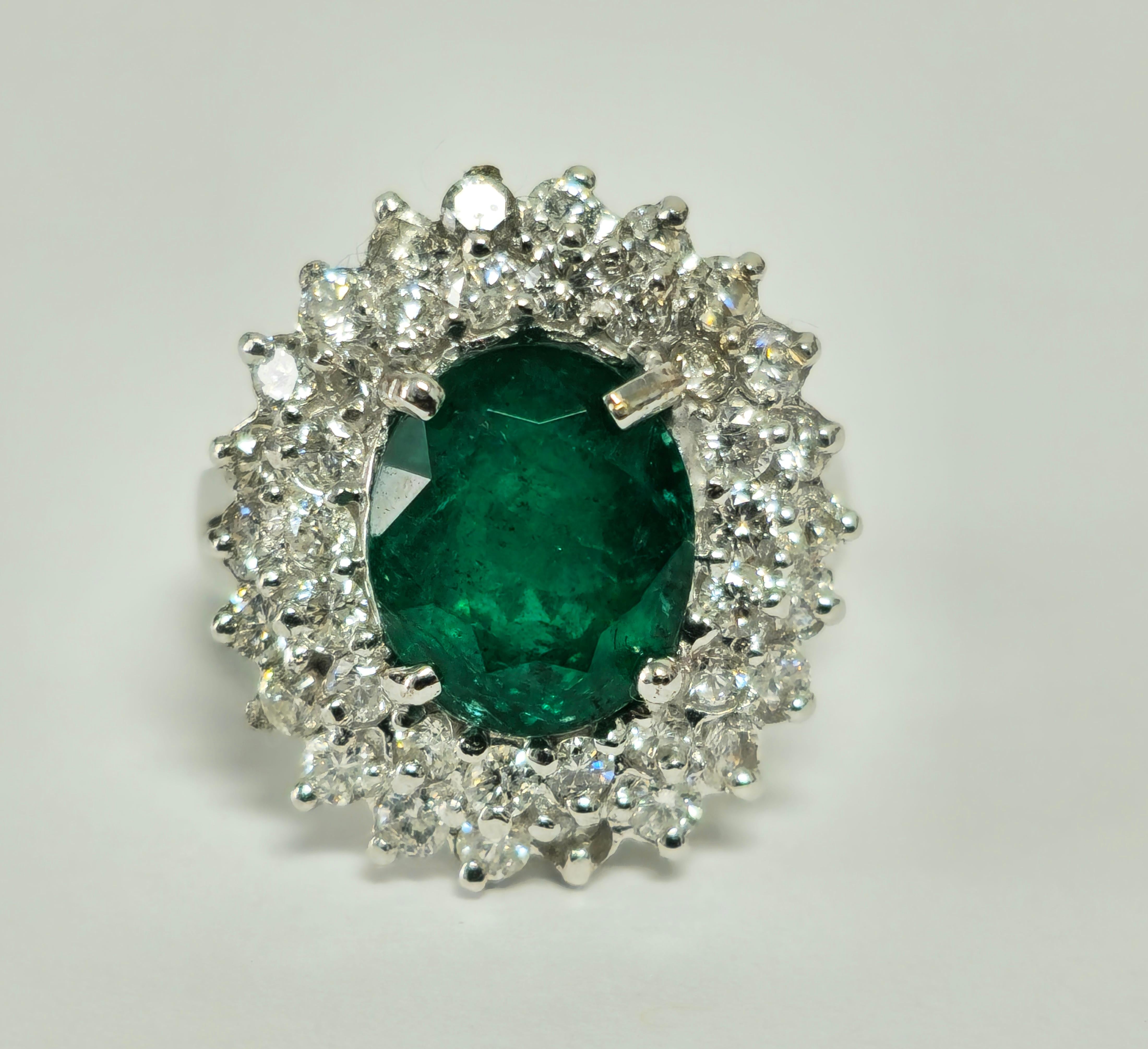 In luxurious 14k white gold, this exquisite cocktail ring features a stunning 3.05 carat oval-shaped emerald, displaying deep color and saturation, securely set in prongs. Encircling the emerald are 1.50 carats of round brilliant cut diamonds,