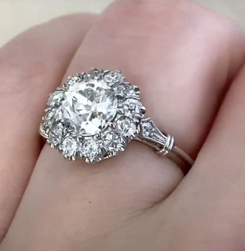 This exquisite cluster ring showcases a GIA-certified old European cut diamond at its center, weighing approx. 1.5-carats. The diamond exhibits a warm J color and SI2 clarity, radiating vintage charm with its distinct faceting. Encircling the center