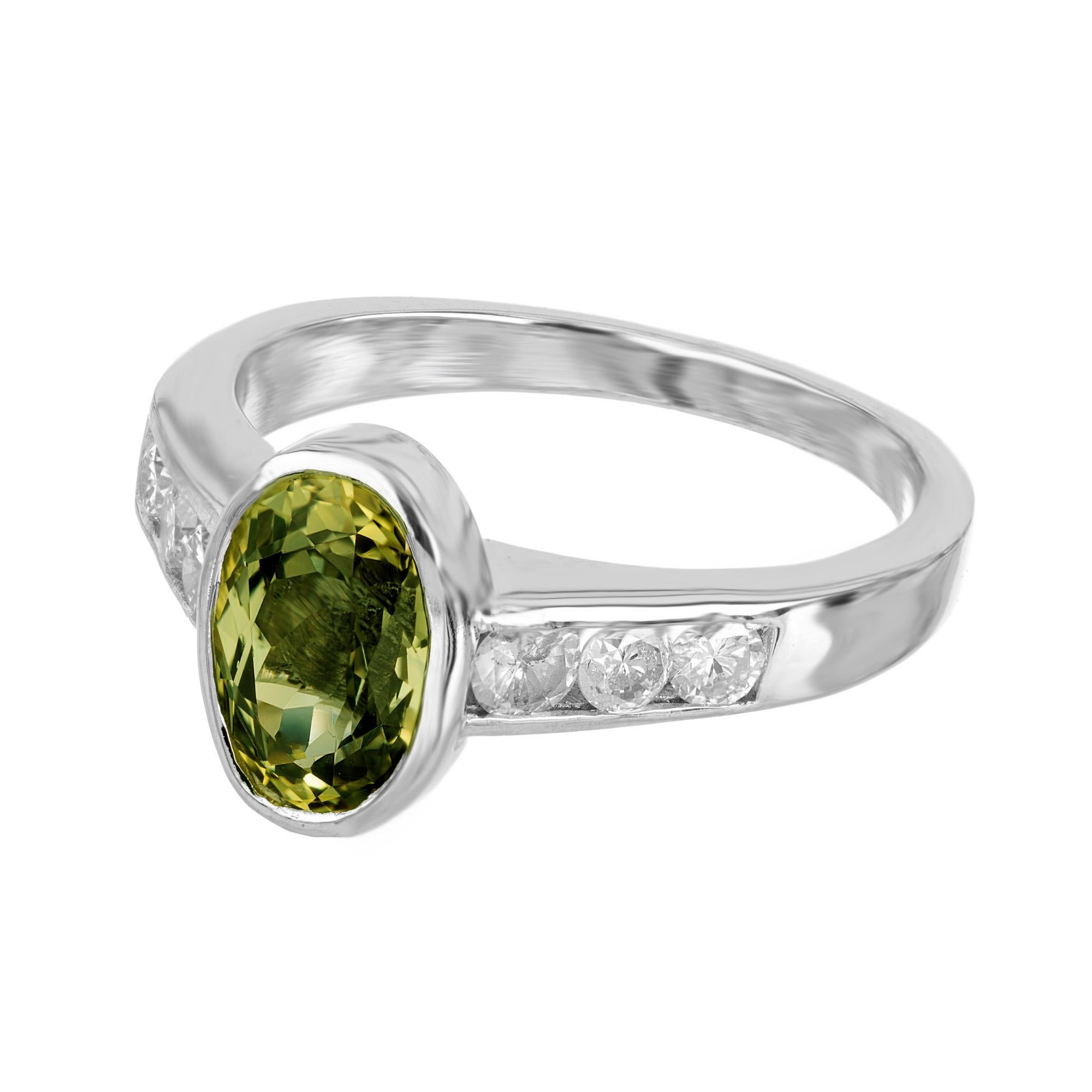 Immerse yourself in the luxurious 1960's oval 2.20 carat green yellow sapphire engagement ring. A true masterpiece, this ring offers a brilliant symphony of colors. The captivating bezel set oval-shaped sapphire, with its striking blend of green and