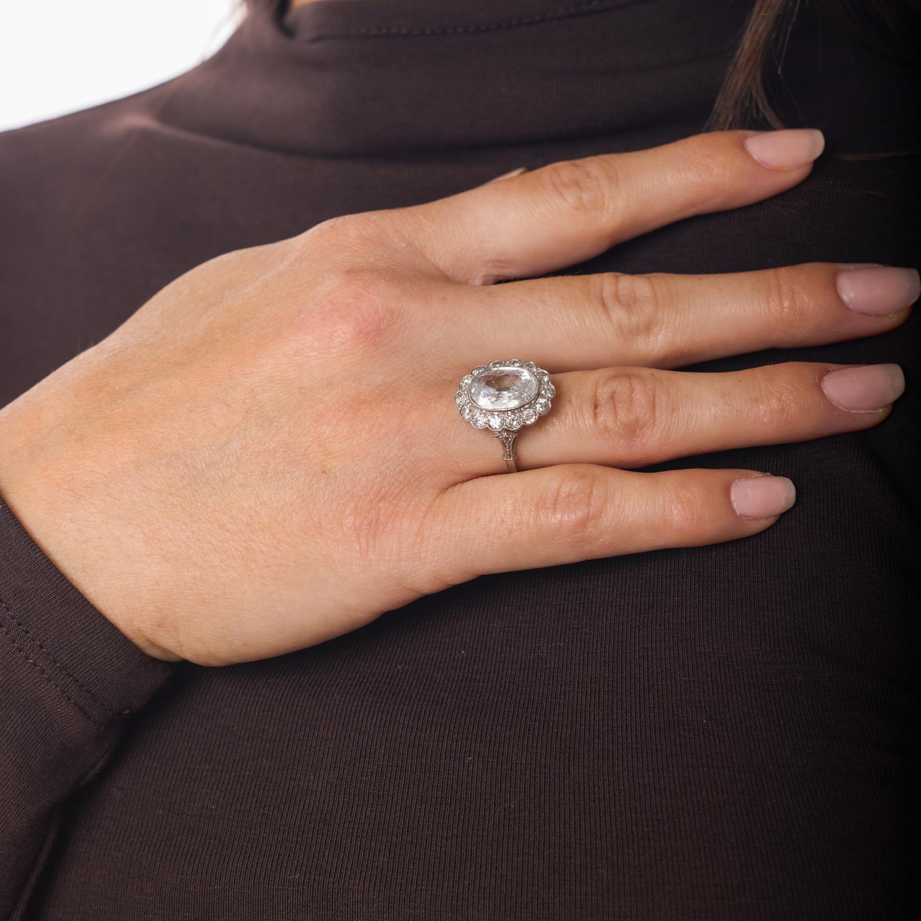 Questo anello a grappolo in platino è incentrato su un sorprendente diamante taglio old mine da 3,02 carati, la cui tonalità di colore F brillante e le ampie sfaccettature antiche creano una presenza luminosa che sembra allo stesso tempo storica e
