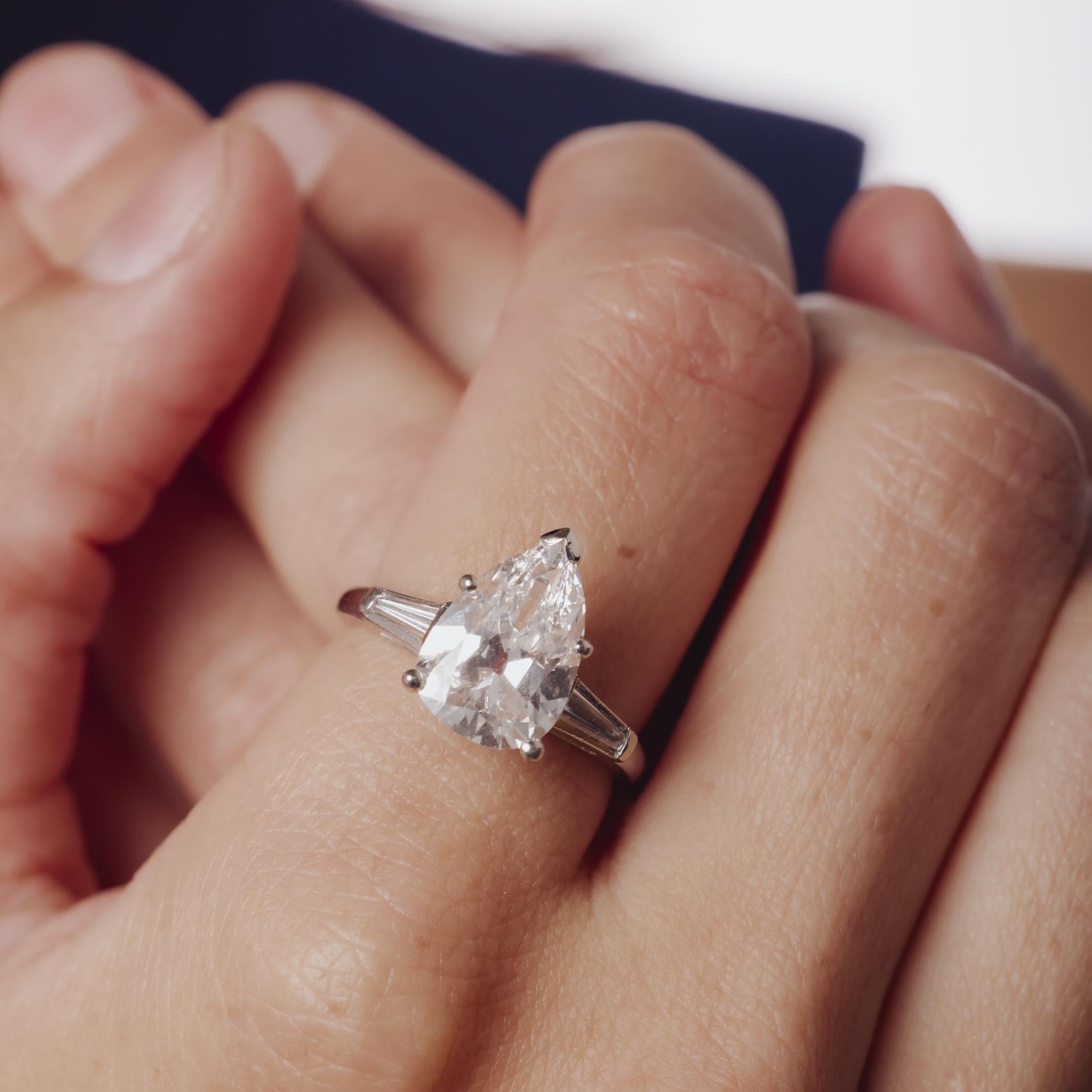 Cette bague en platine du milieu du siècle met en valeur un superbe diamant poire de 3,02 ct d'origine ancienne d'une brillance exceptionnelle, flanqué de baguettes effilées pour une élégance raffinée et intemporelle.