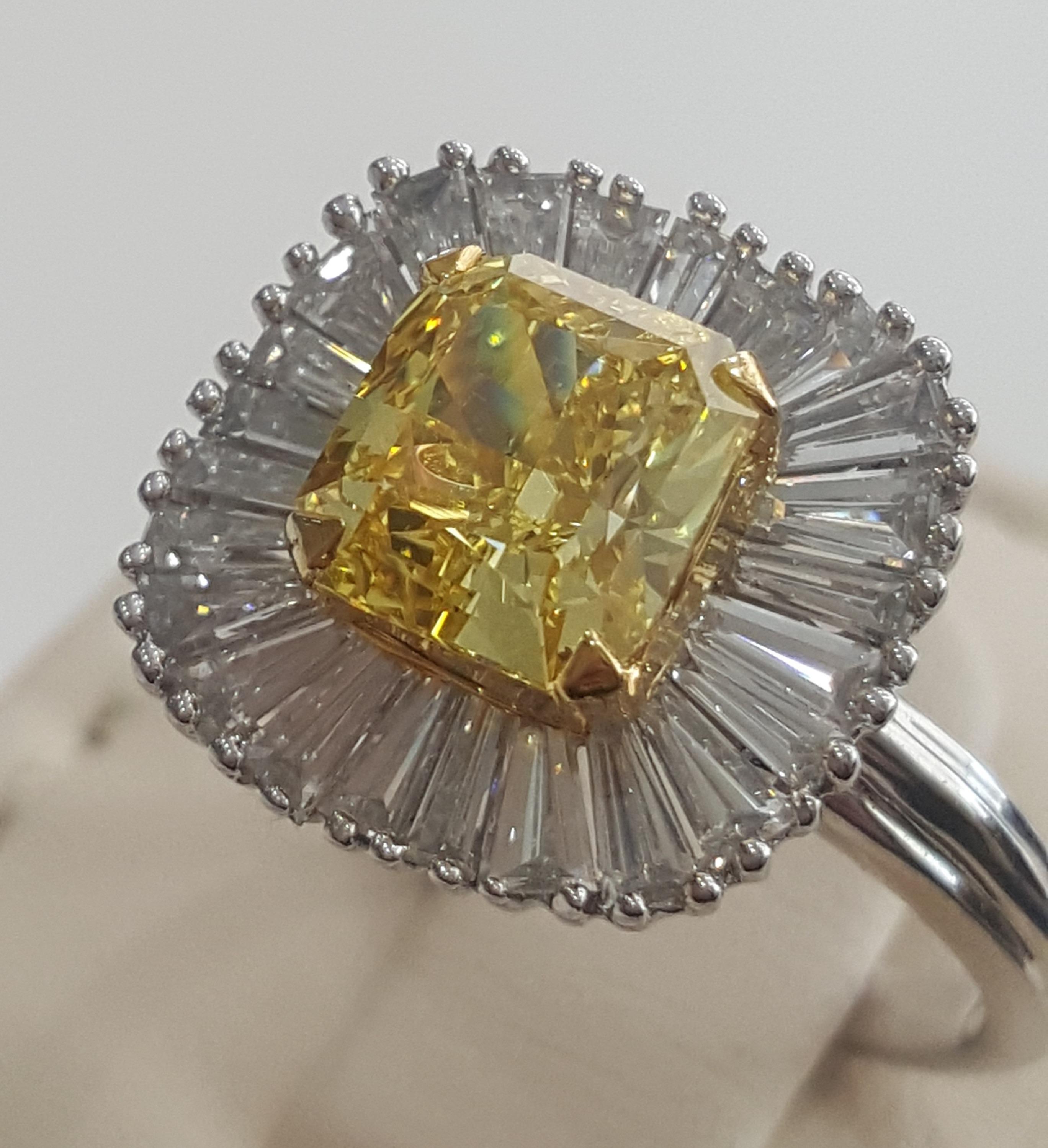 This understated, elegant and enticing ring created by Moguldiam Inc in 18 k white gold features a GIA certified natural fancy vivid yellow Radiant weighing 2.02 carat with VS2 clarity with a halo of tapered baguette accent diamonds weighing 1.10