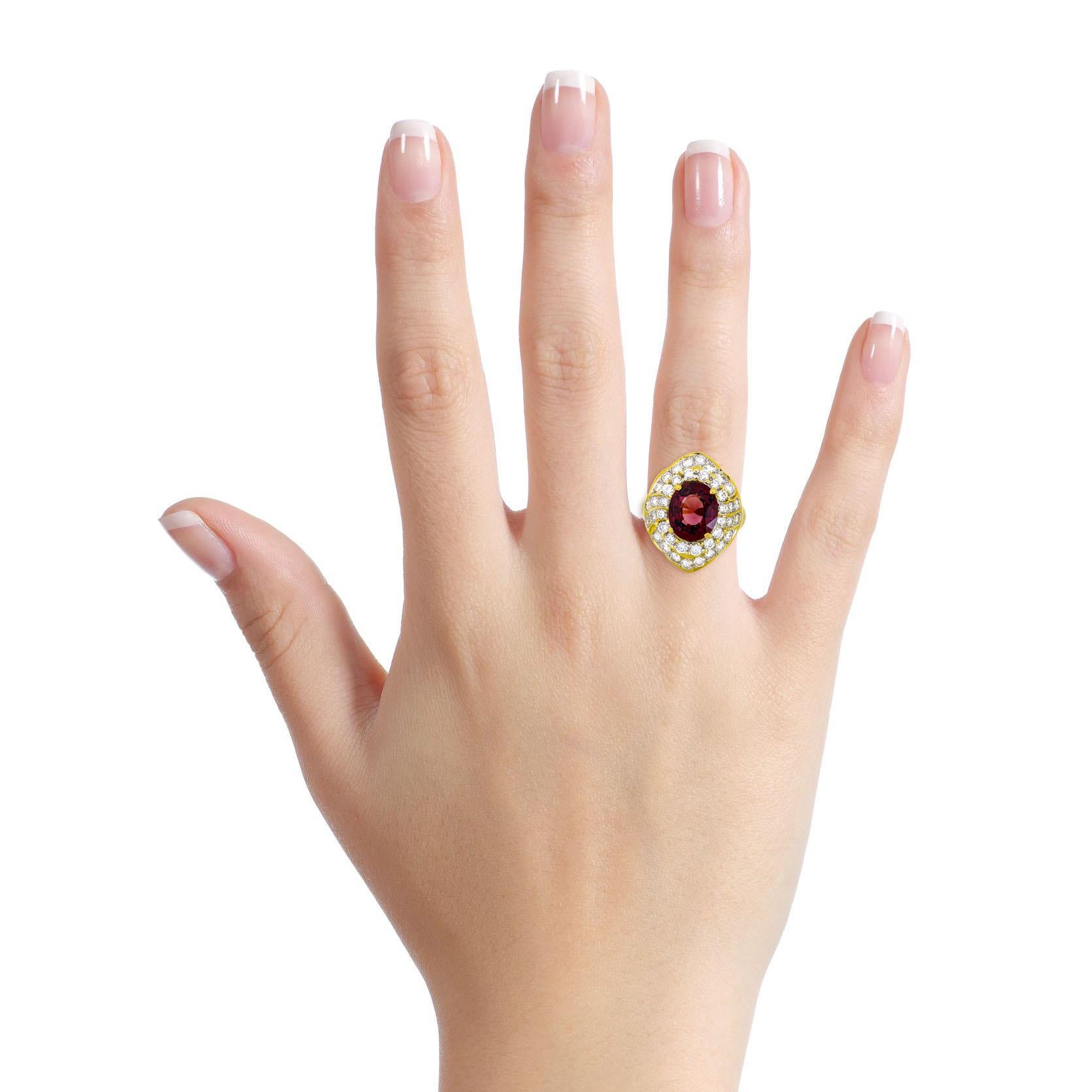 Red spinel and diamond cocktail ring in 18-karat yellow gold. Polished metal setting with an oval-cut unheated natural red spinel at the center surrounded by numerous near-colorless round-cut diamonds. The spinel weighs 3.25 carats and comes with a