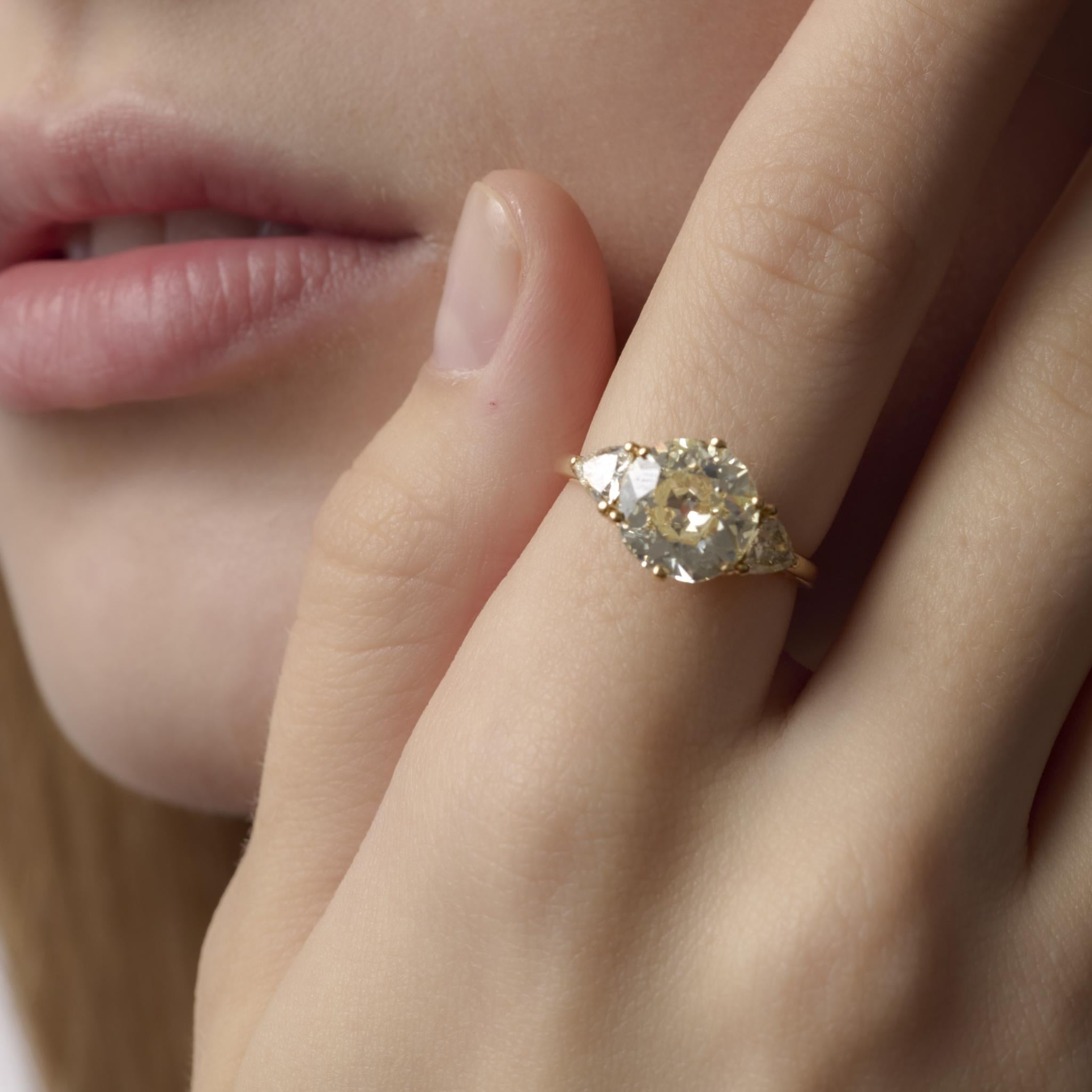 Questo anello vintage degli anni '80 sfoggia un diamante di taglio europeo da 3,35 carati incorniciato da pietre laterali di taglio trilione, che irradia calore ed eleganza senza tempo in oro giallo 18 carati.