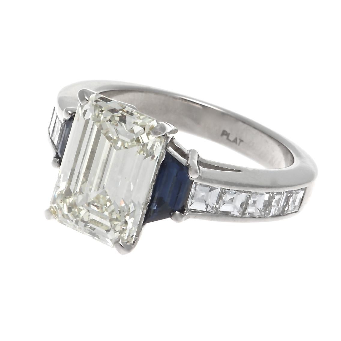 It's all champagne and sunshine with this GIA 3.44 carat O-P color, VS2 prong set emerald cut diamond ring. Framed by two perfectly suited faceted trapezoid cut sapphires and channel set square emerald cuts on the platinum band. Size 5 1/2, sizing