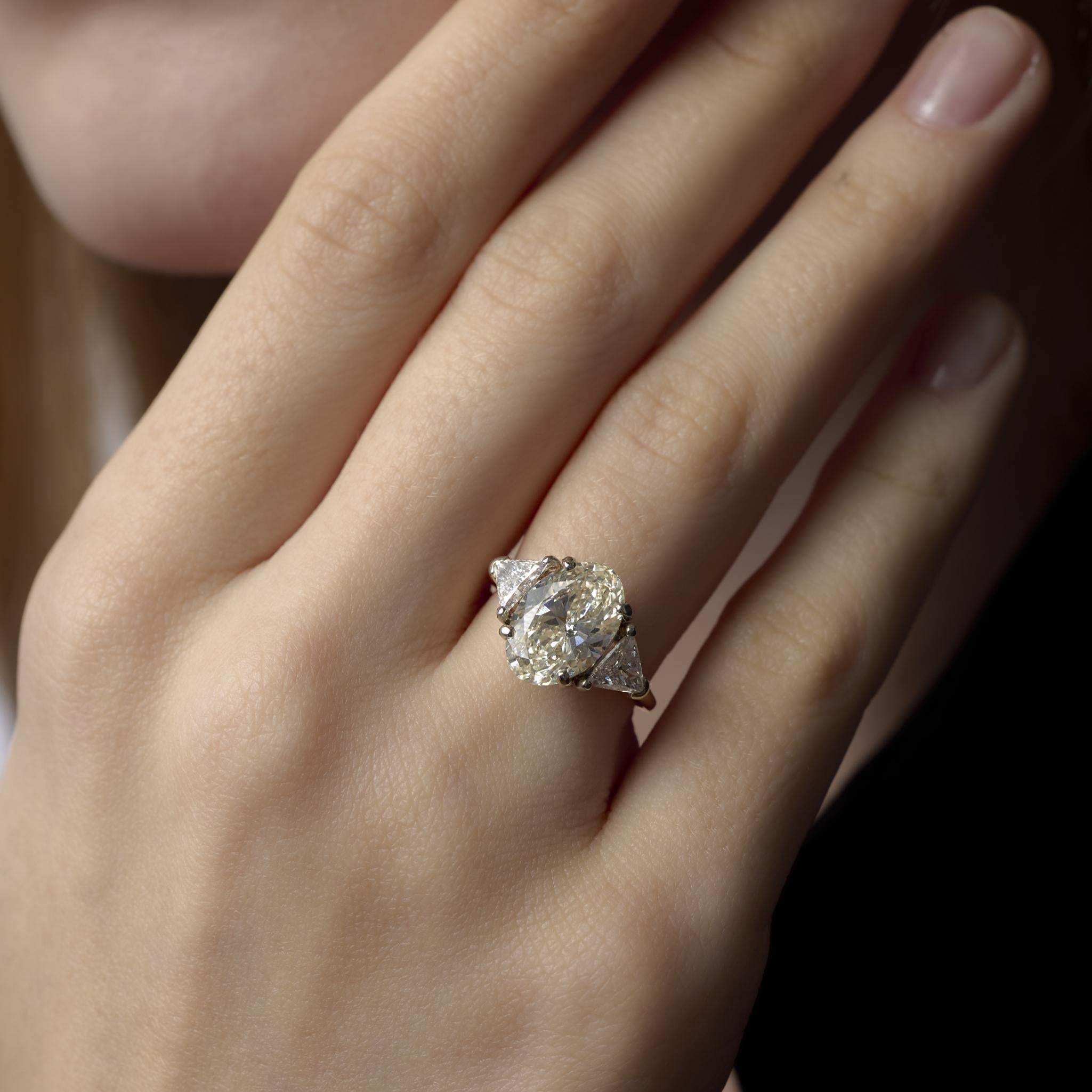 Cette bague vintage des années 1990 en or bicolore présente un diamant ovale GIA de 4,01 carats encadré par des côtés rayonnants taillés en trillion, offrant un mélange saisissant de chaleur et de brillance.