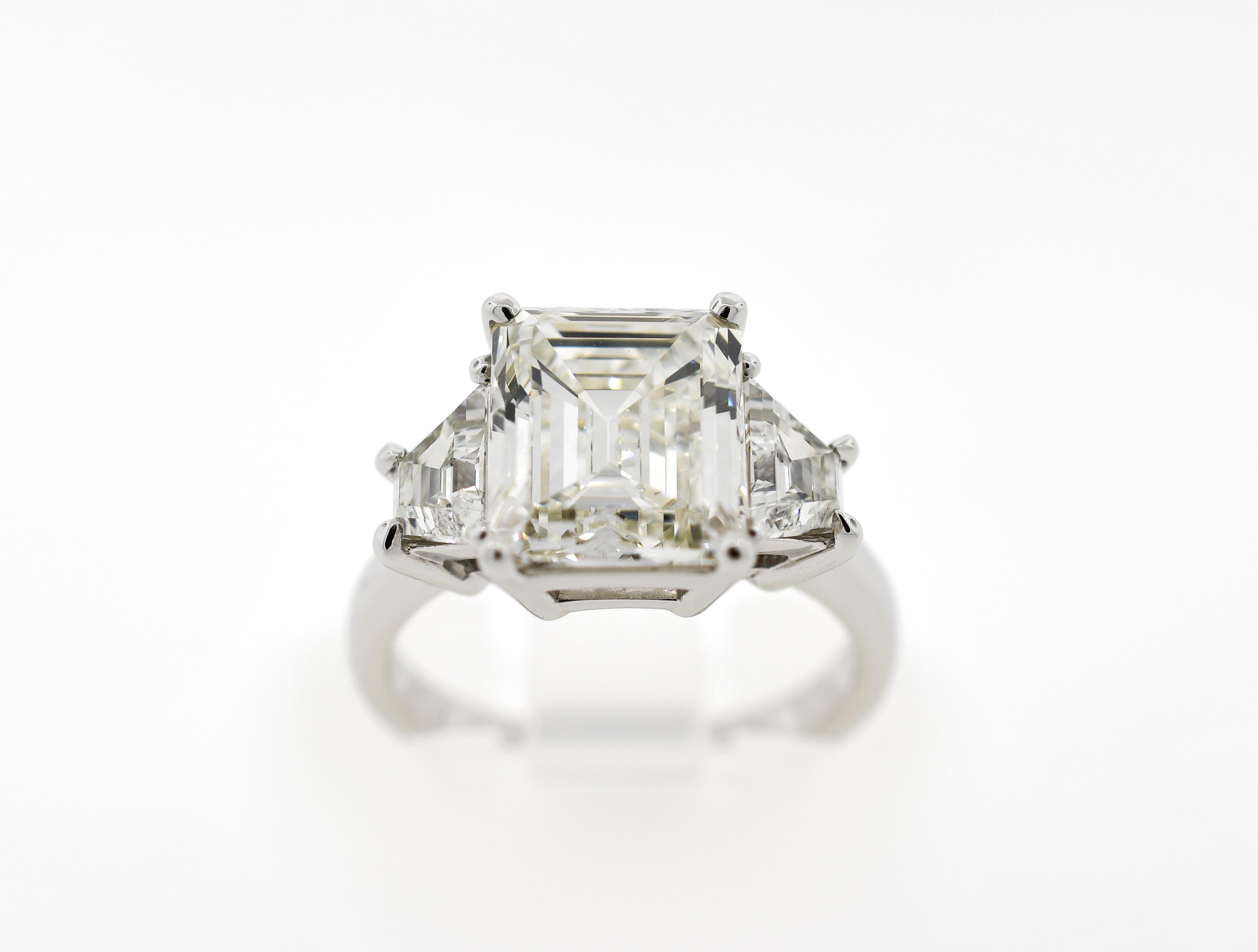 Custom made platinum three stone contemporary mounting, centered by one (1) emerald cut diamond weighing 4.05 carats, flanked by two (2) trapezoid cut diamonds weighing .94 carats total weight, VS1 clarity, H color.  Finger size 6.25
Center stone