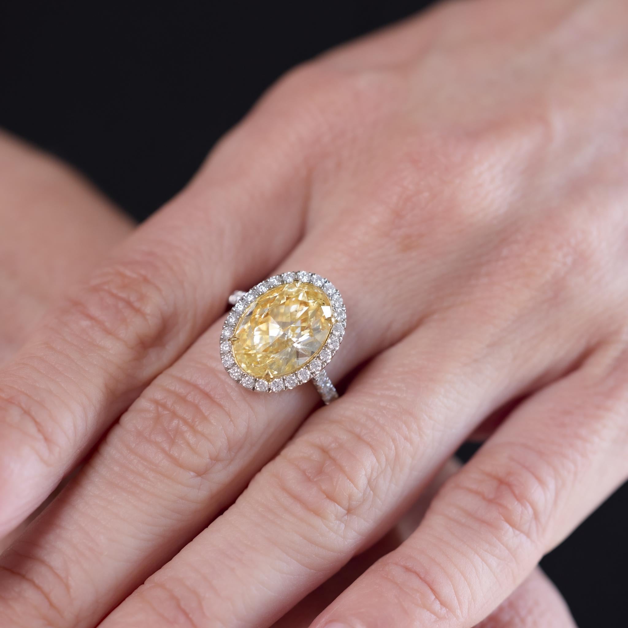 Cette bague moderne des années 2020 est ornée d'un diamant de taille ovale de 5,07 carats, certifié par le GIA (#2235463037) de couleur Fancy Light Yellow et de pureté SI2. La pierre centrale est rehaussée de 46 diamants ronds de taille brillant
