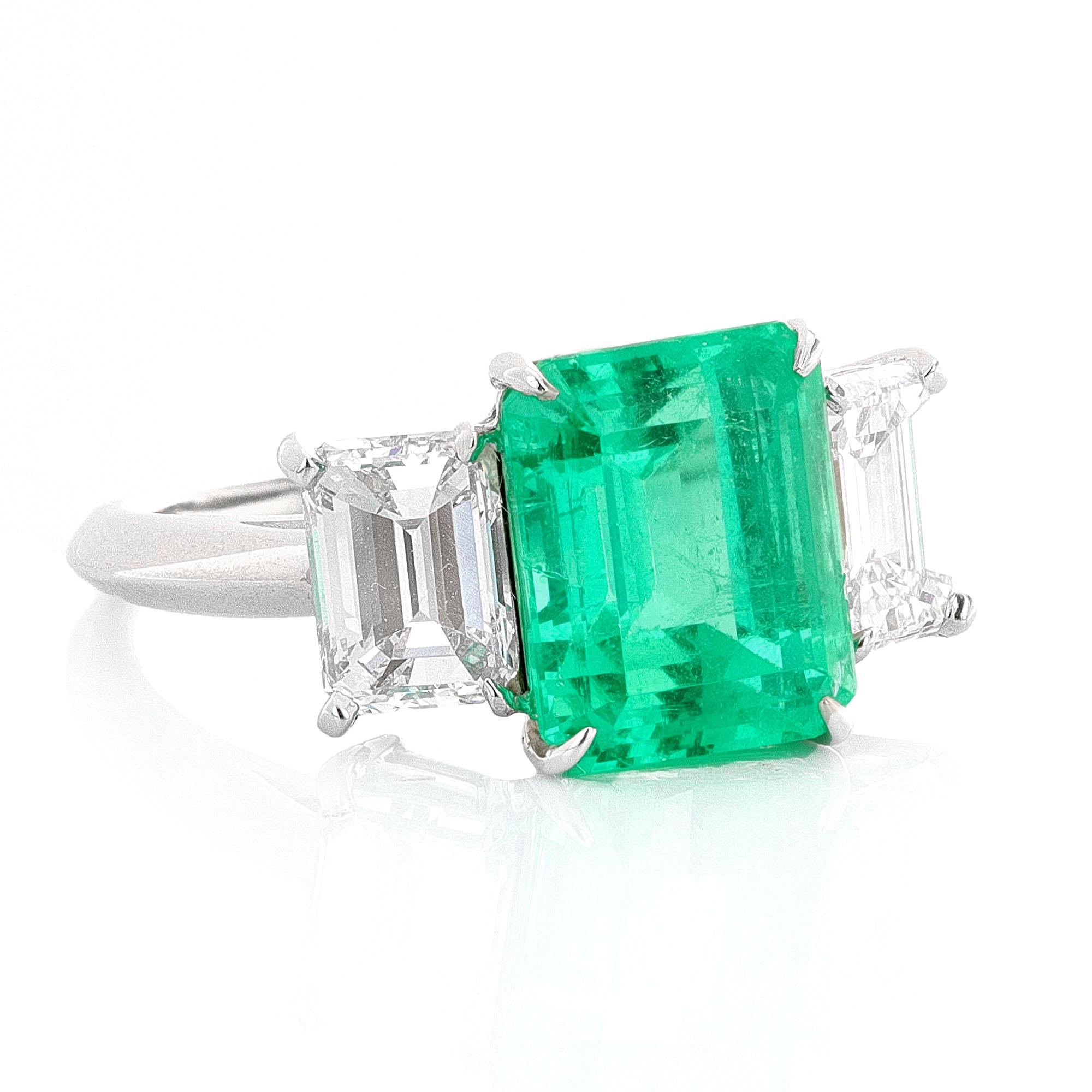 Platinum three stone emerald ring with diamond side stones. The center stone is AGL certified and the side stones are GIA certified. AGL describes the center stone as a 4.27 carat, emerald cut emerald. The emerald is natural, green, and has Minor