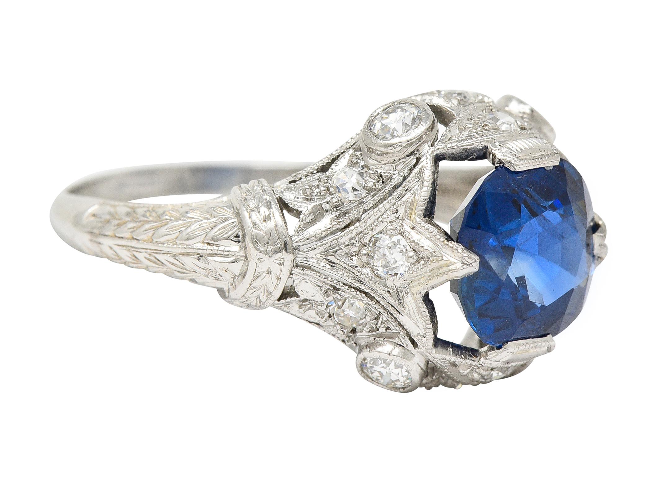 Centering a cushion cut sapphire weighing 2.61 carats total - transparent medium blue. Natural Cambodian in origin with no indications of heat treatment - set with tab prongs. Flanked by fleur-de-lis motif shoulders and decorus surround. Accented by