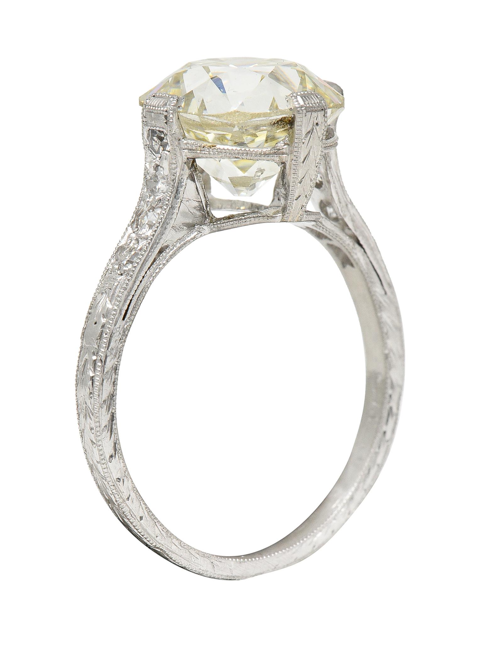 Centering an old European cut diamond weighing 3.44 carats - O/P color with VS2 clarity. Set with tab-like prongs in a decorously engraved wheat motif basket. Flanked by cathedral shoulders bead set with single cut diamonds. Weighing approximately