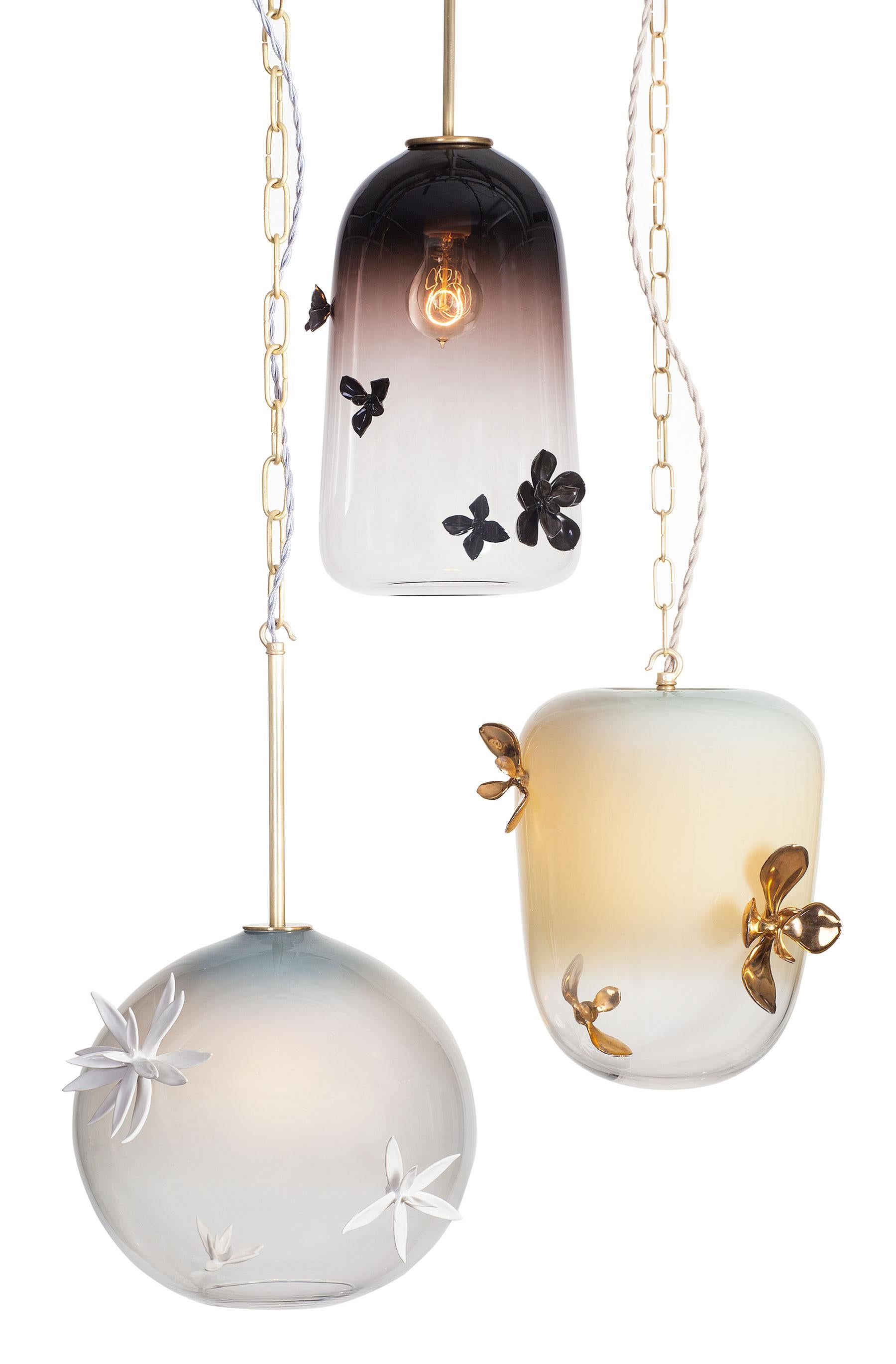 La colección de iluminación Gia se compone de vidrio soplado adornado con plantas de porcelana hechas a mano. Las piezas de cristal se ofrecen en tres formas: globo, linterna o campana.  Los adornos de porcelana hechos a mano se moldean a partir de
