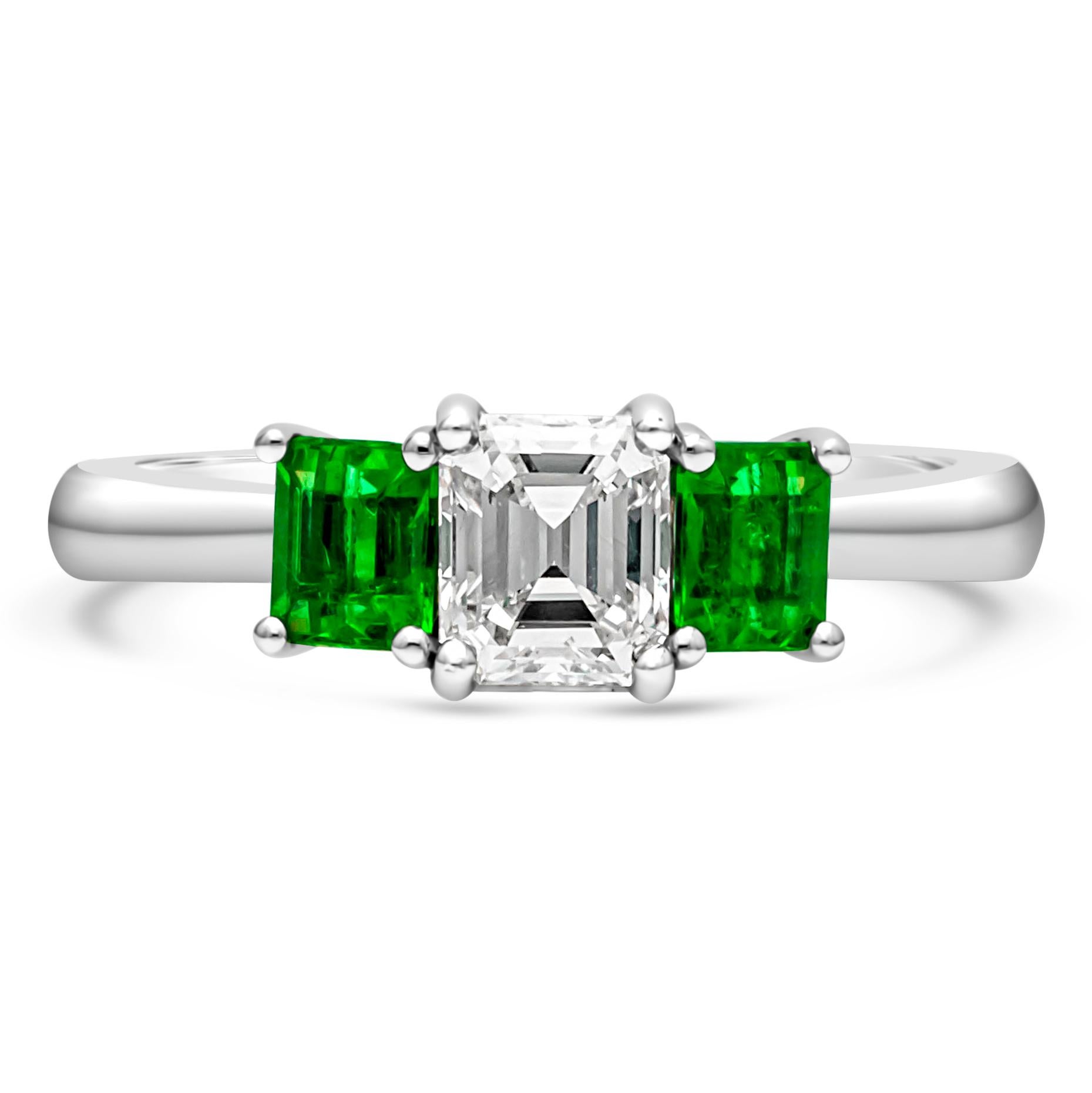 A simple three-stone engagement ring style, showcasing a 0.71 carat emerald cut diamond certified by GIA as F color and VS2 clarity. Flanked by emerald cut green emeralds weighing 0.60 carat total. Each stone is set on a four prong open gallery