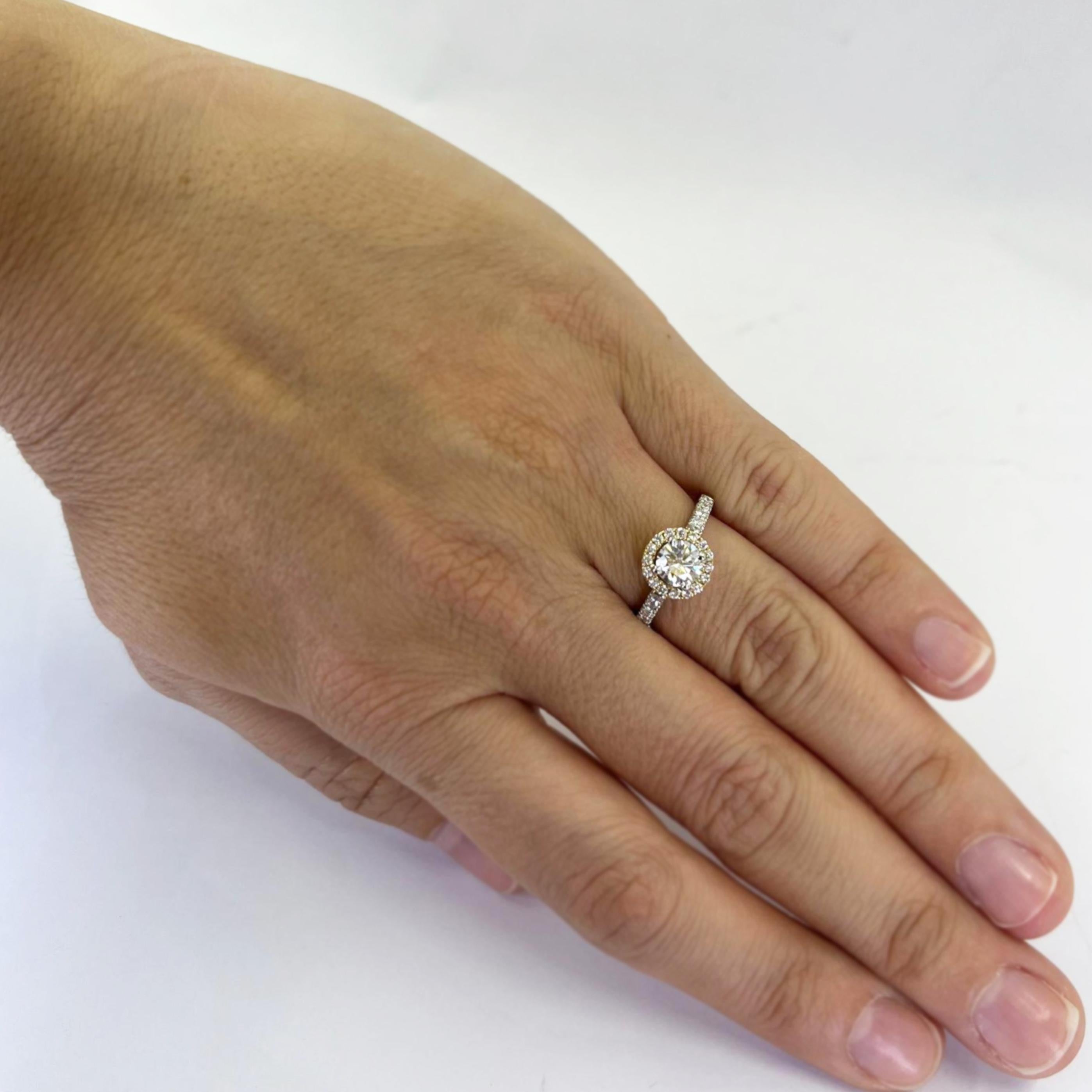 Platinum and 18 karat yellow gold halo ring featuring a 0.71 carat round brilliant cut diamond GIA graded (report #1308475631) as E color and VVS1 clarity with excellent cut, polish, and symmetry. The ring also contains 26 pave-set round brilliant