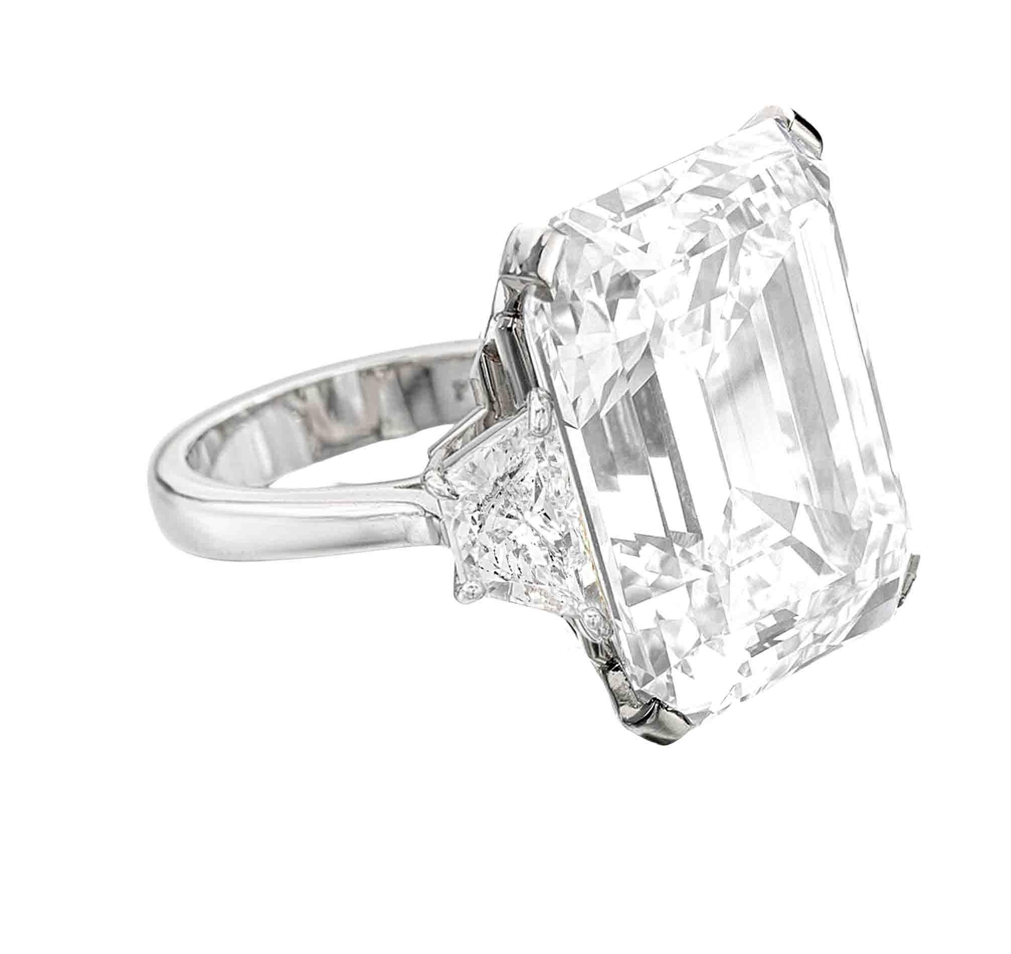 This magnificent engagement ring features a breathtaking 10.02 carat emerald cut diamond, GIA certified for its exceptional quality. The step cut facets of the center stone create a mesmerizing hall of mirrors effect, enhancing its depth and