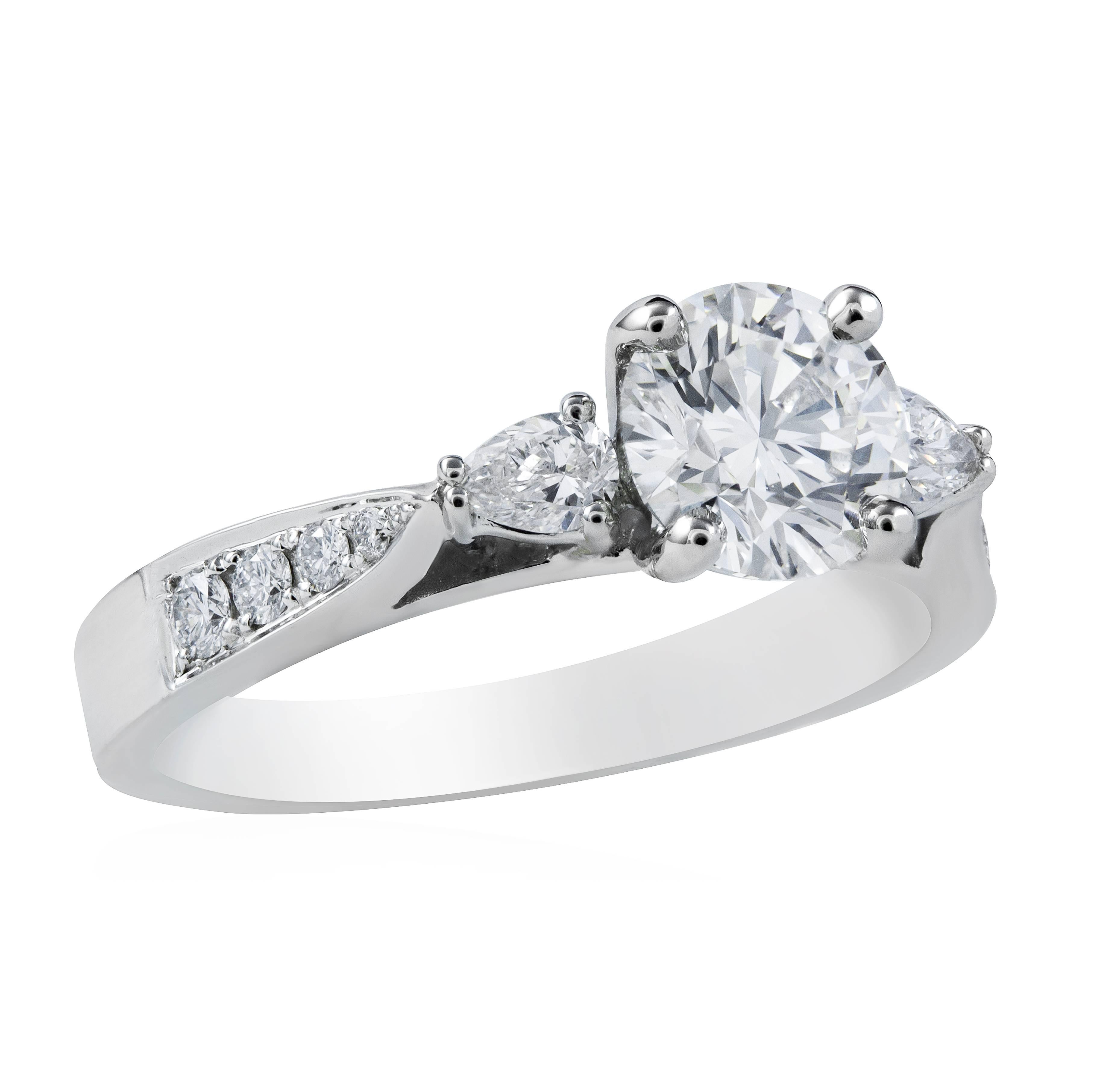 A timeless diamond engagement ring, showcasing a 1.00 carat round brilliant cut diamond certified by GIA as H color and VS2 clarity, set on a four prong setting. Elegantly flanked by pear shape diamonds weighing 0.23 carat total and accented by a