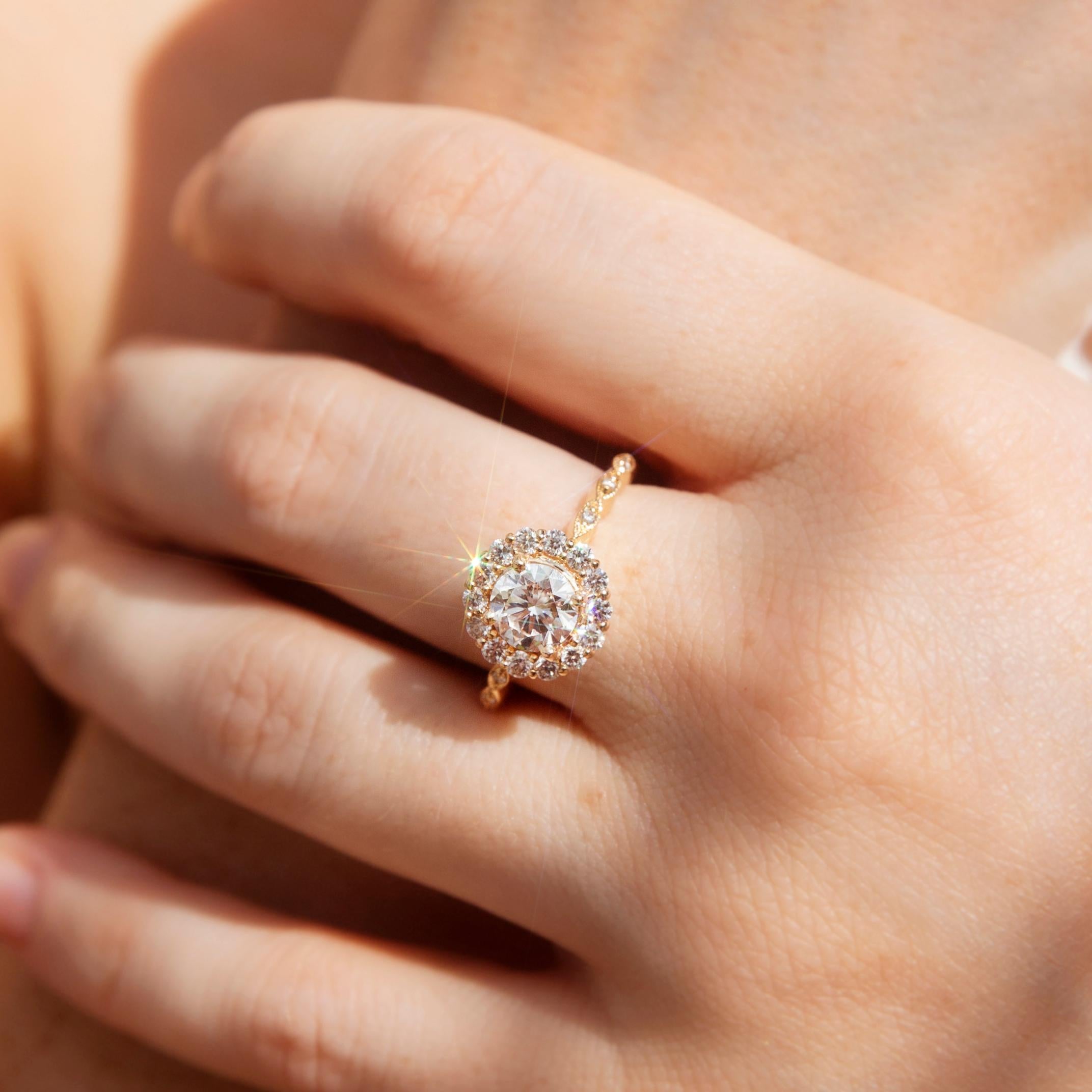 Lovingly crafted in 18 carat yellow gold, this scintillating vintage-inspired halo cluster ring features a gorgeous 1.01-carat GIA-certified round brilliant cut diamond. Around the centrepiece is an enchanting halo border of round brilliant cut