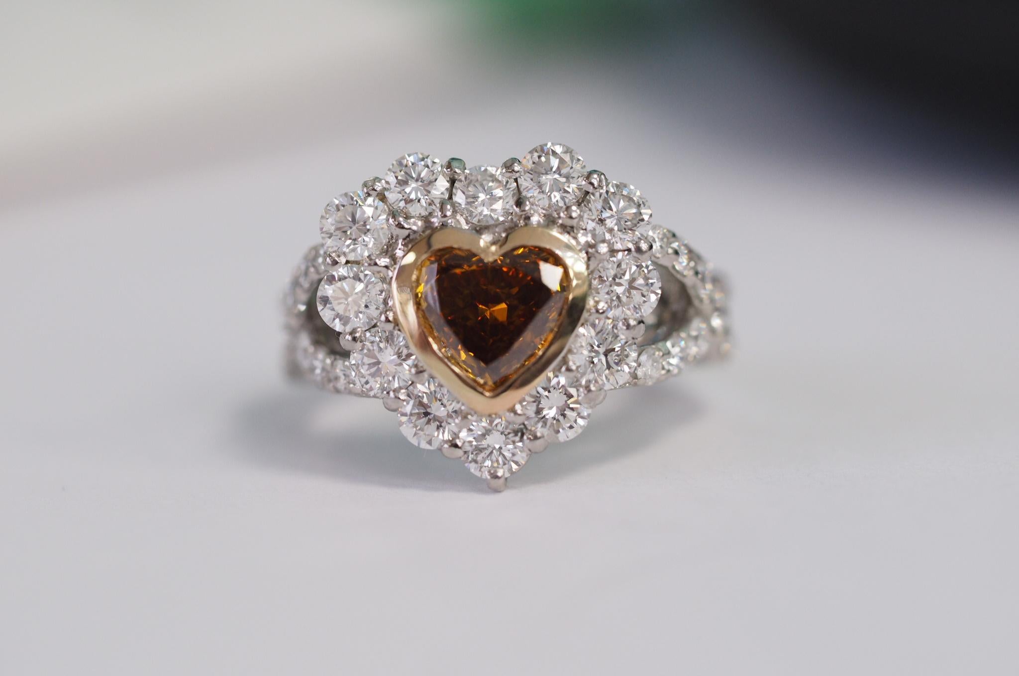 This Center is a Natural, fancy deep brownish yellowish orange Heart diamond with GIA certificate, no.1308992514. It weighs 1.01 carats and is  SI2  in clarity. The dimensions are 6.54 x 7.05 x 3.04mm. It is bezel set with 18k yellow gold. This ring