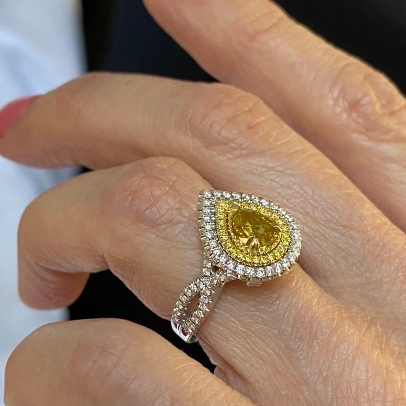 This dazzling, one-of-a-kind engagement ring is a true statement piece, featuring a 1.01-carat GIA Certified natural fancy deep brownish yellow pear-shaped diamond (Report Number #2171208532) with measurements of 6.64 x 5.77 x 3.37 mm. The exquisite