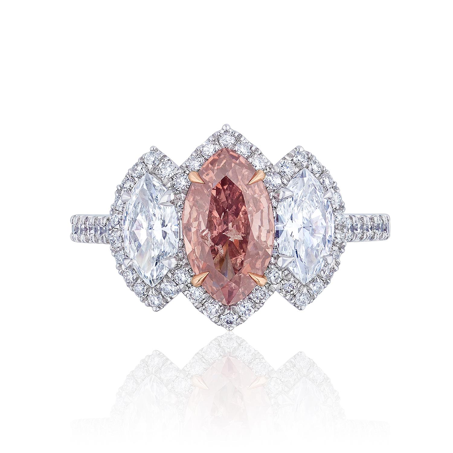 Marquise shaped Diamond weighing 1.01 Carats with GIA certificate stating the diamond is Fancy Deep Orangy Pink. Very unique color.

Flanked by Marquise shaped white Diamonds weighing 0.80 Carats of F color and VS Clarity.

Set in Platinum. Center