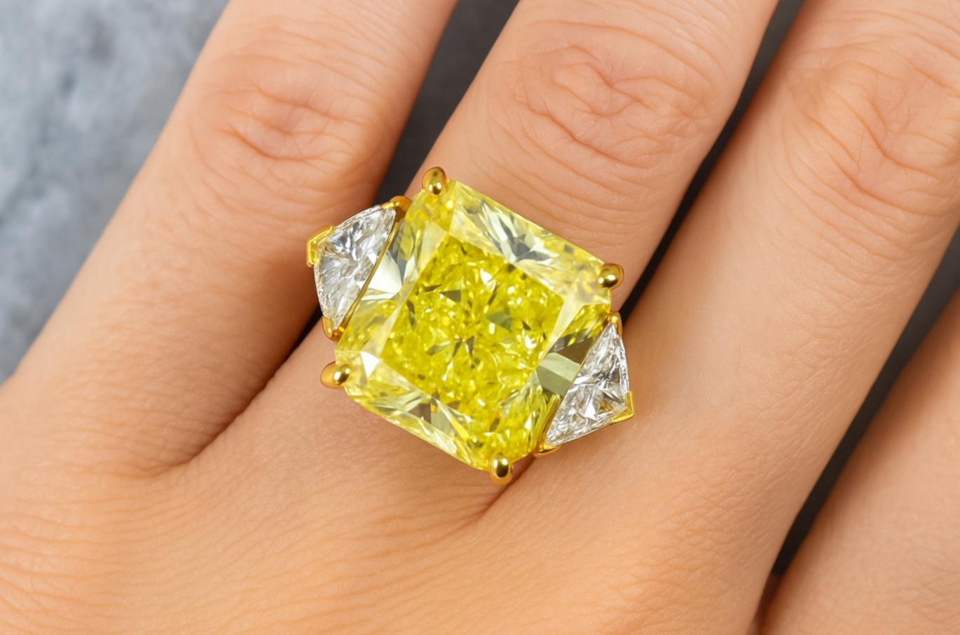 A dramatic and rare 10.12 carat Fancy Yellow diamond takes center stage in this bold statement ring, certified by GIA. The cut-cornered rectangular modified brilliant cut exhibits exceptional brilliance and an even distribution of rich yellow color,