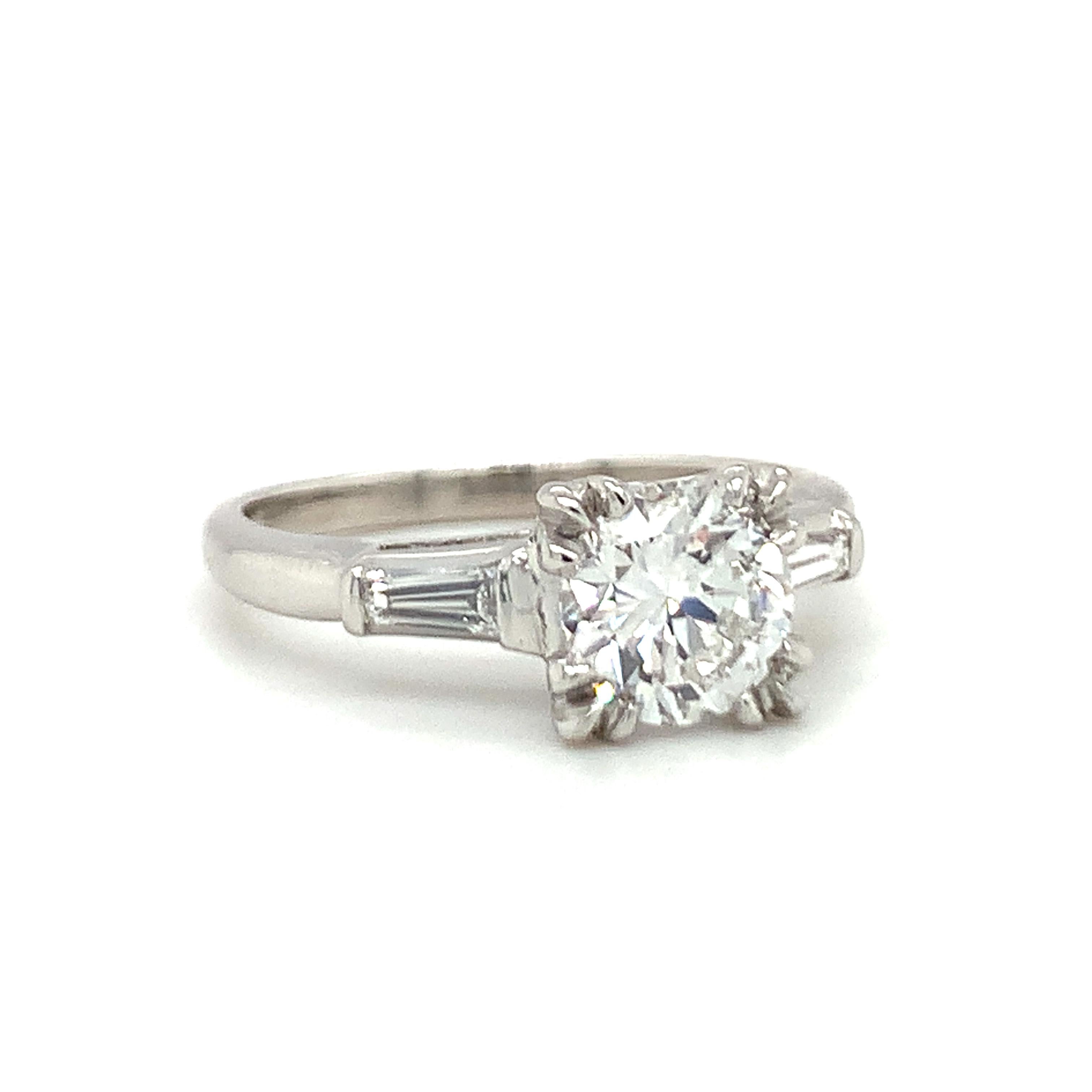 Ein GIA-zertifizierter Verlobungsring aus Platin mit einem 1,04-karätigen Diamanten im Brillantschliff mit einem Gewicht von 1,04 Karat, Farbe E und Reinheit VS-1. Der Hauptdiamant wird flankiert von zwei spitz zulaufenden Baguette-Diamanten mit