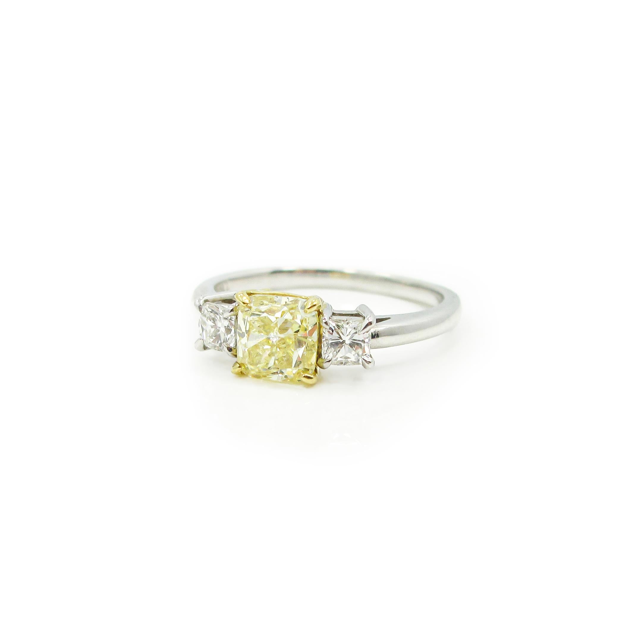 The center stone is a fancy yellow cushion cut diamond weighing 1.04ct. and is accompanied by GIA certification. The yellow diamond is set in an 18k yellow gold basket between two cushion cut diamonds weighing approximately 0.31ct total weight, F to